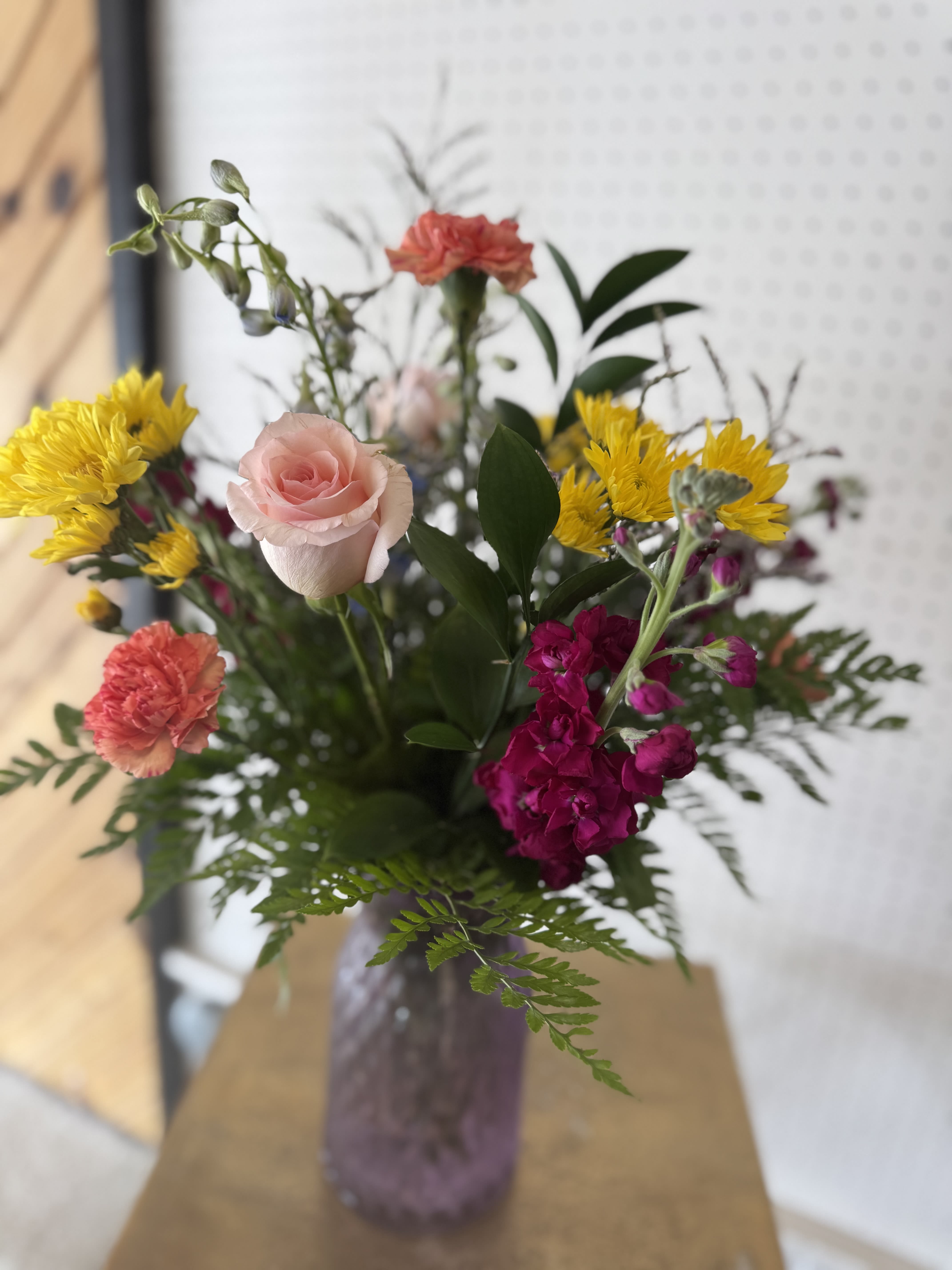 Love you Bunches Bouquet - A cheerful Mother’s Day bouquet filled with bright yellow, pink, coral, and fuchsia blooms, arranged with fresh greenery in a soft lavender vase. Sweet, colorful, and full of happy energy — perfect for making Mom smile.
