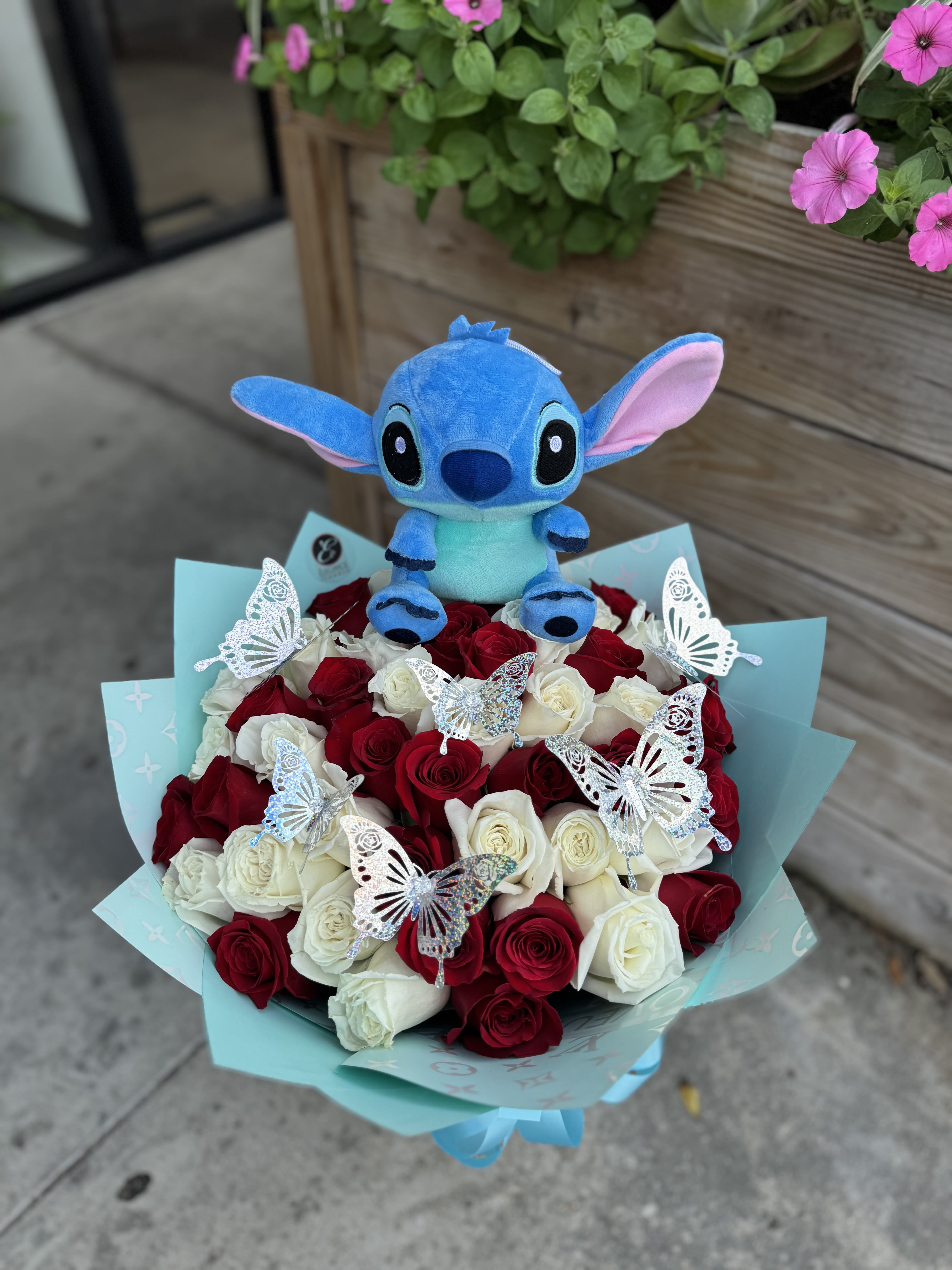 Bouquet of red and white roses with silver butterflies and a blue plush character in aqua wrapping paper