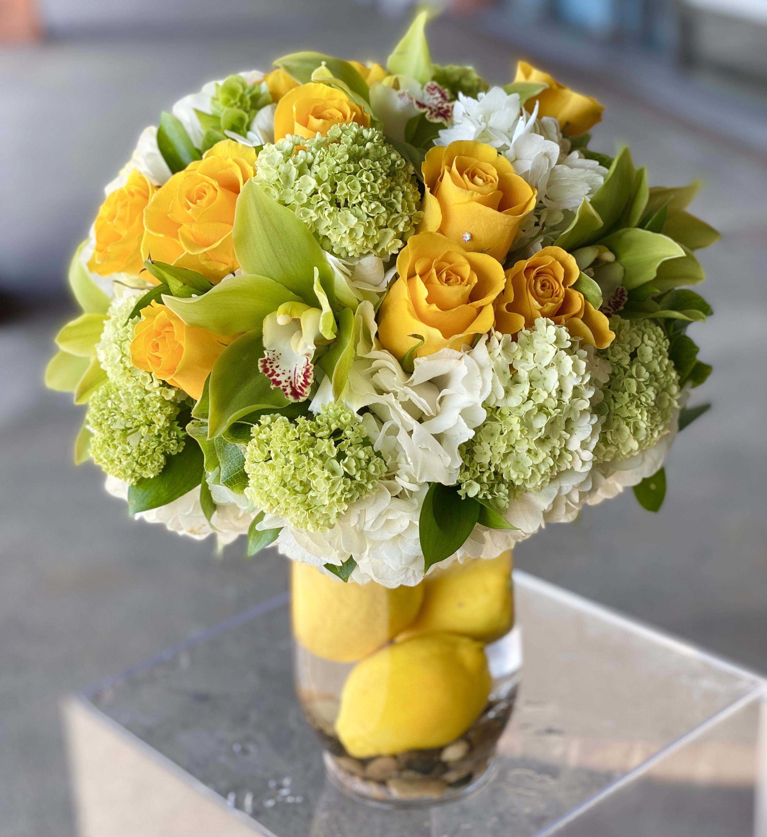 Yellow roses and white flowers arranged in a clear glass vase