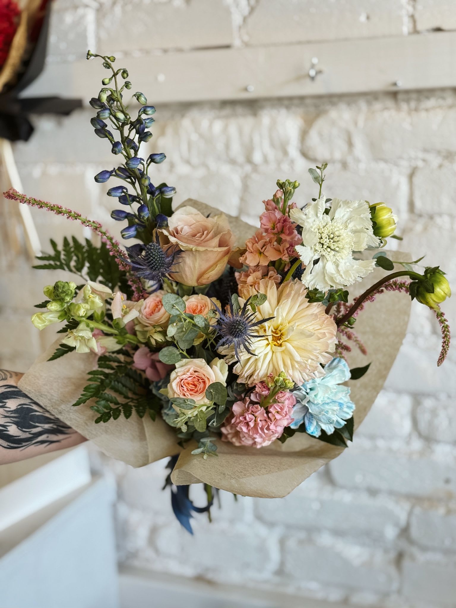 Hand-tied bouquet of pastel flowers wrapped in brown paper