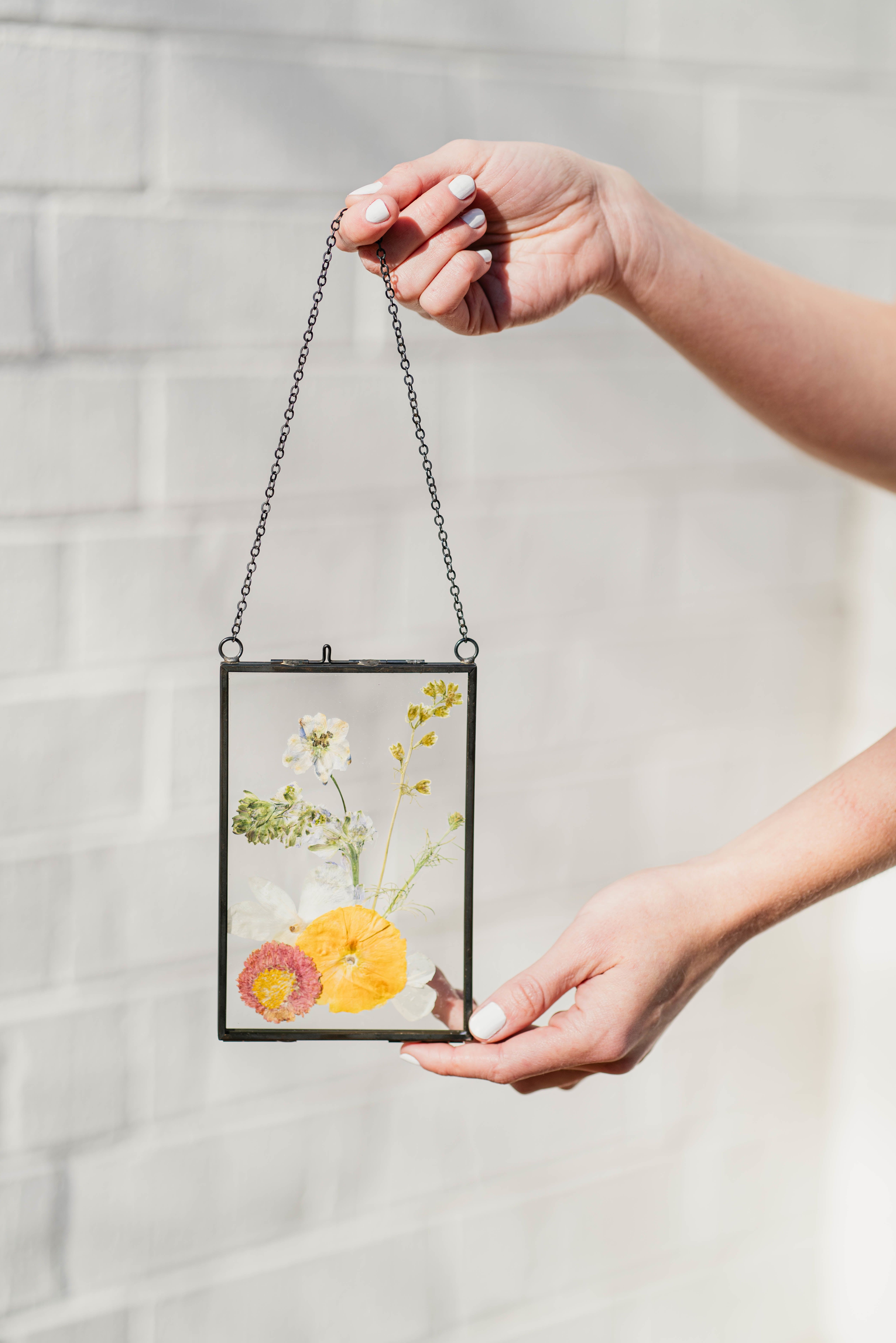 Pressed flowers in a hanging glass frame held by two hands