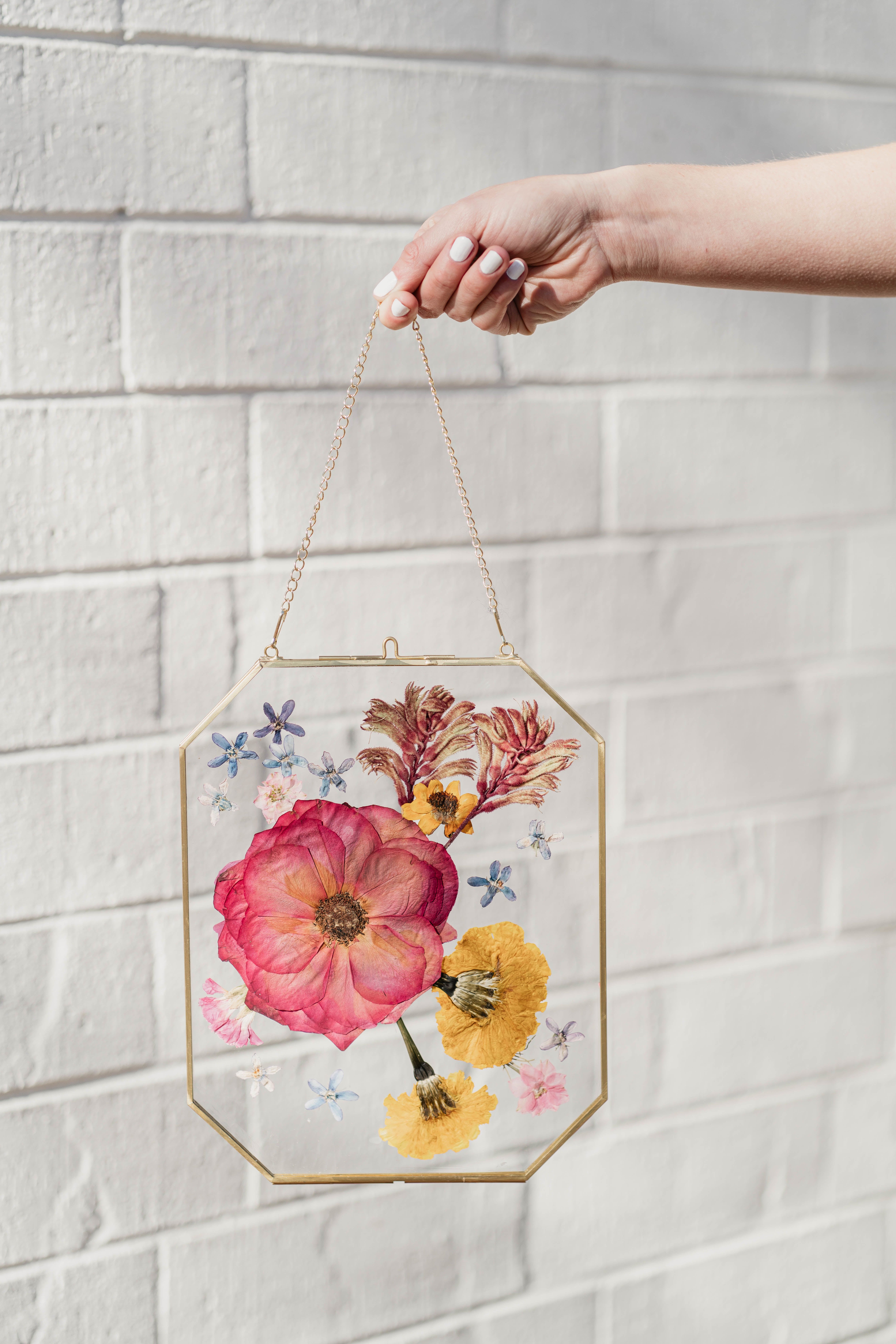 Framed pressed flowers in a hanging glass and brass display