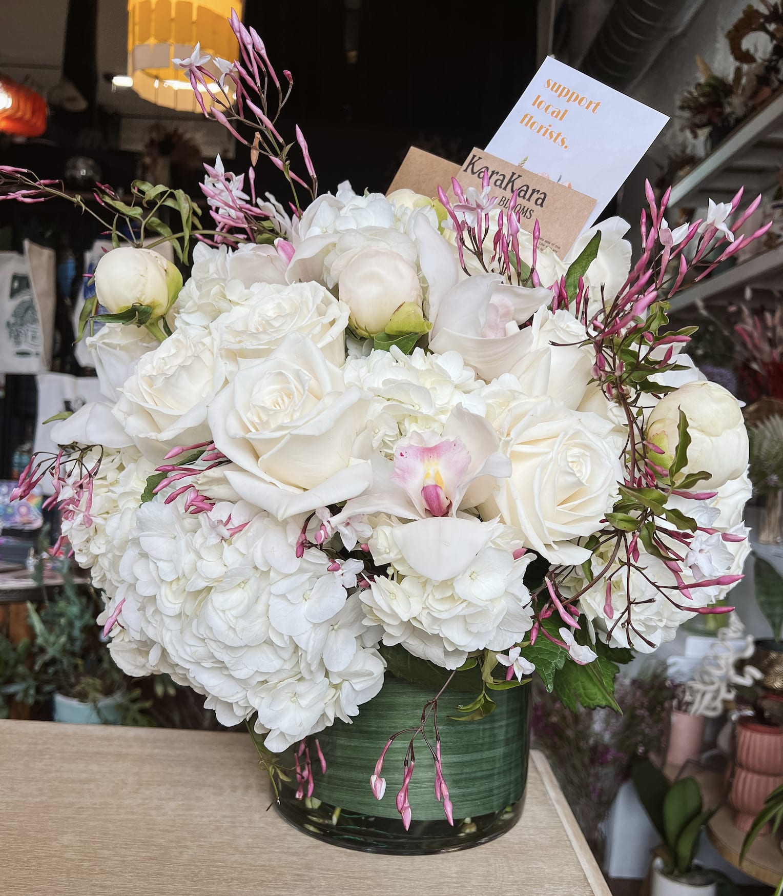 White roses and hydrangeas in a green glass vase with pink accents