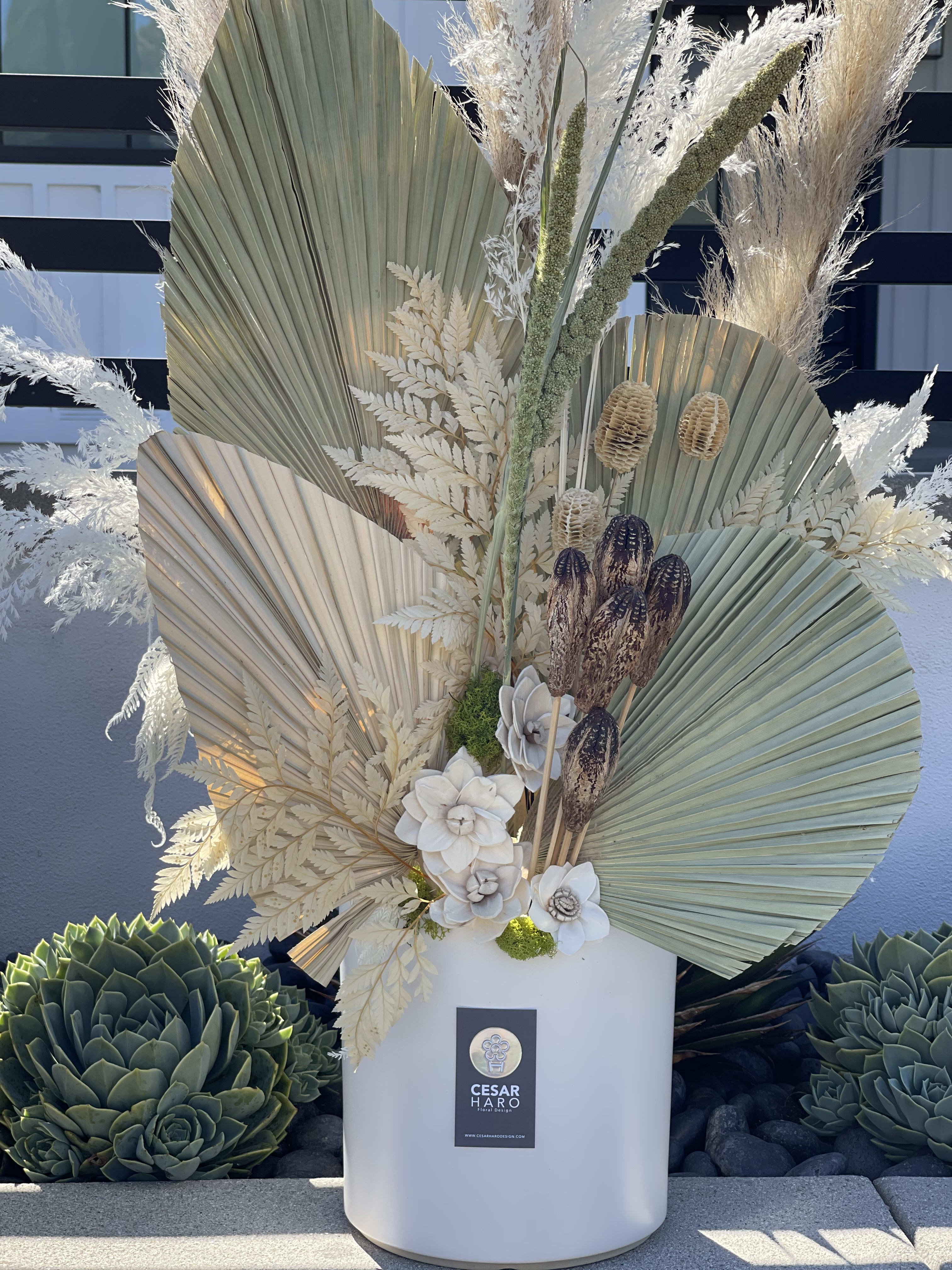 Tall arrangement with dried palm fans, white flowers, and pampas grass in a white vase.