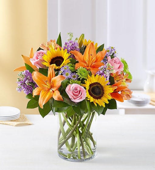 Bouquet of sunflowers, orange lilies, and pink roses in a glass vase