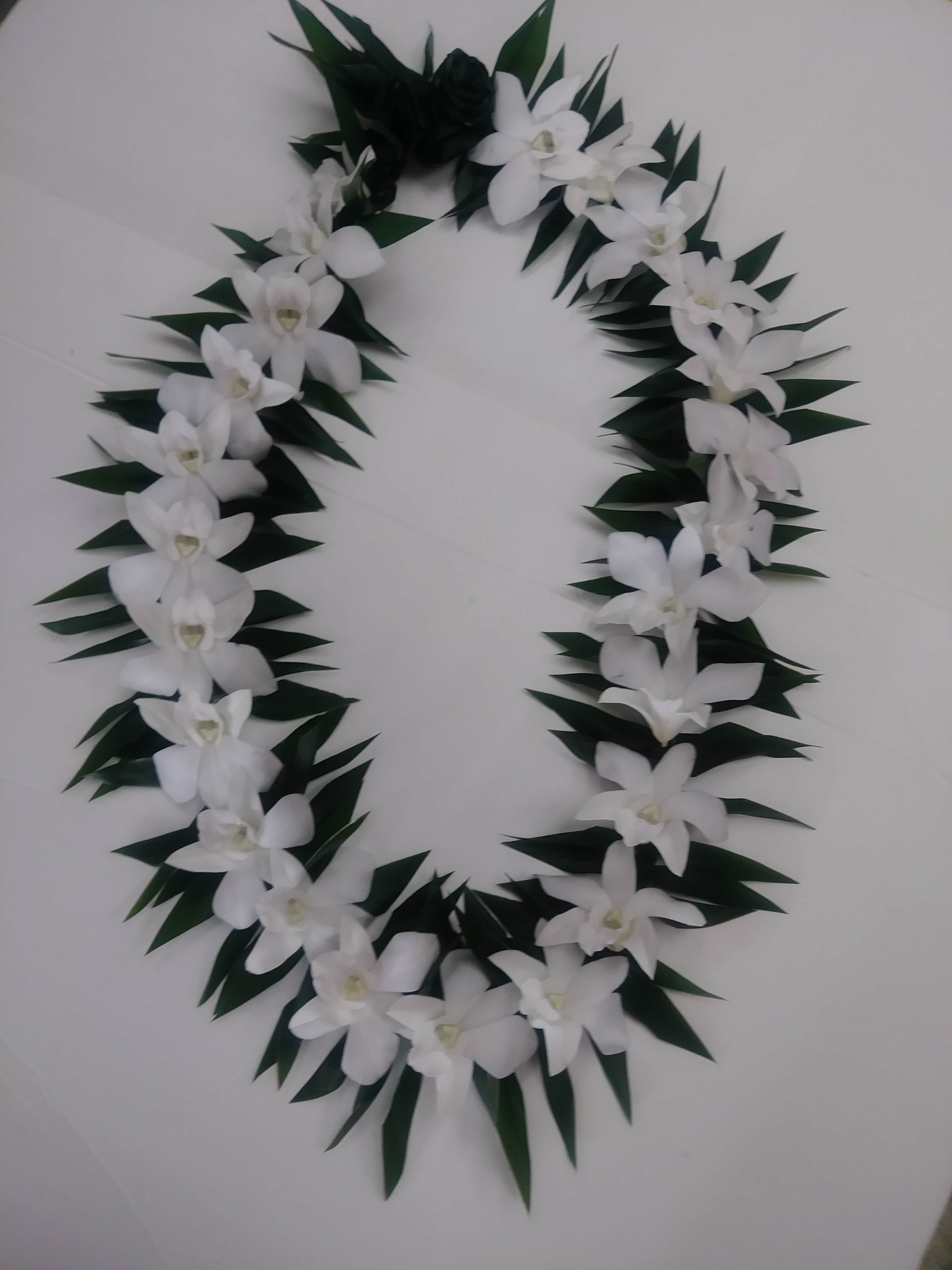 White orchid lei with dark green leaves on a light surface