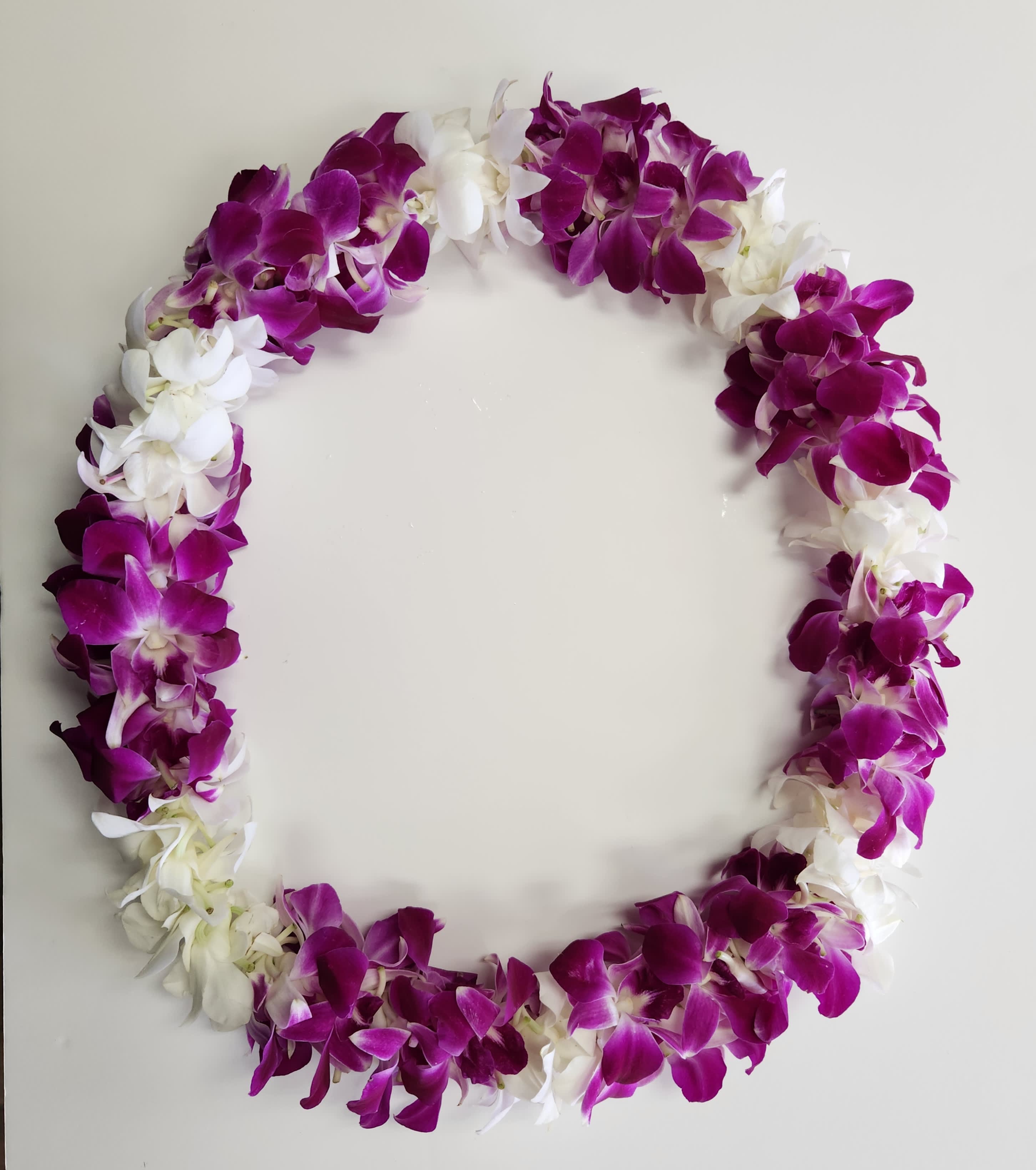 Purple and white orchid lei arranged in an oval shape on a plain light background