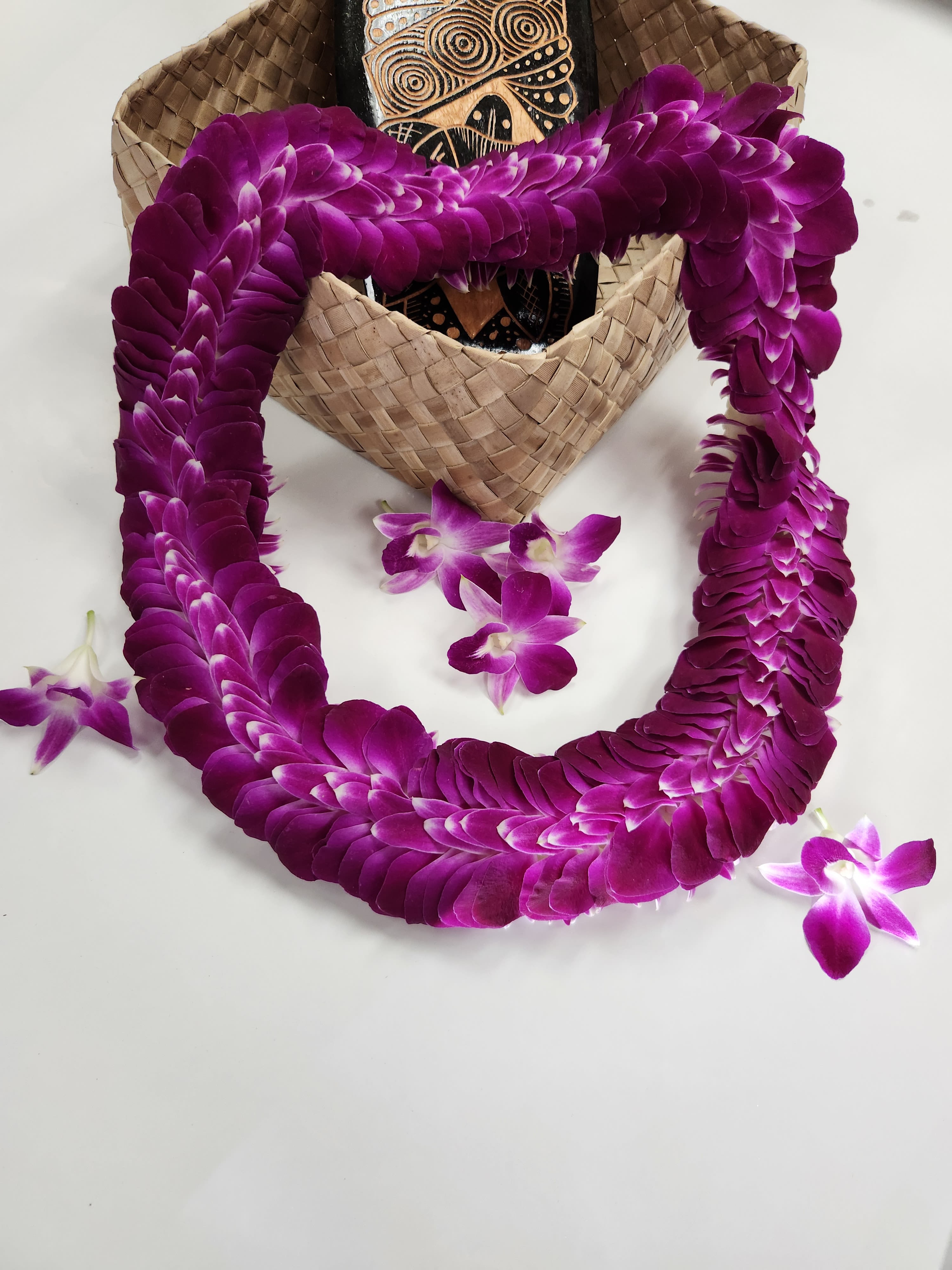 Purple orchid lei draped over a woven hat with a few loose orchid blooms
