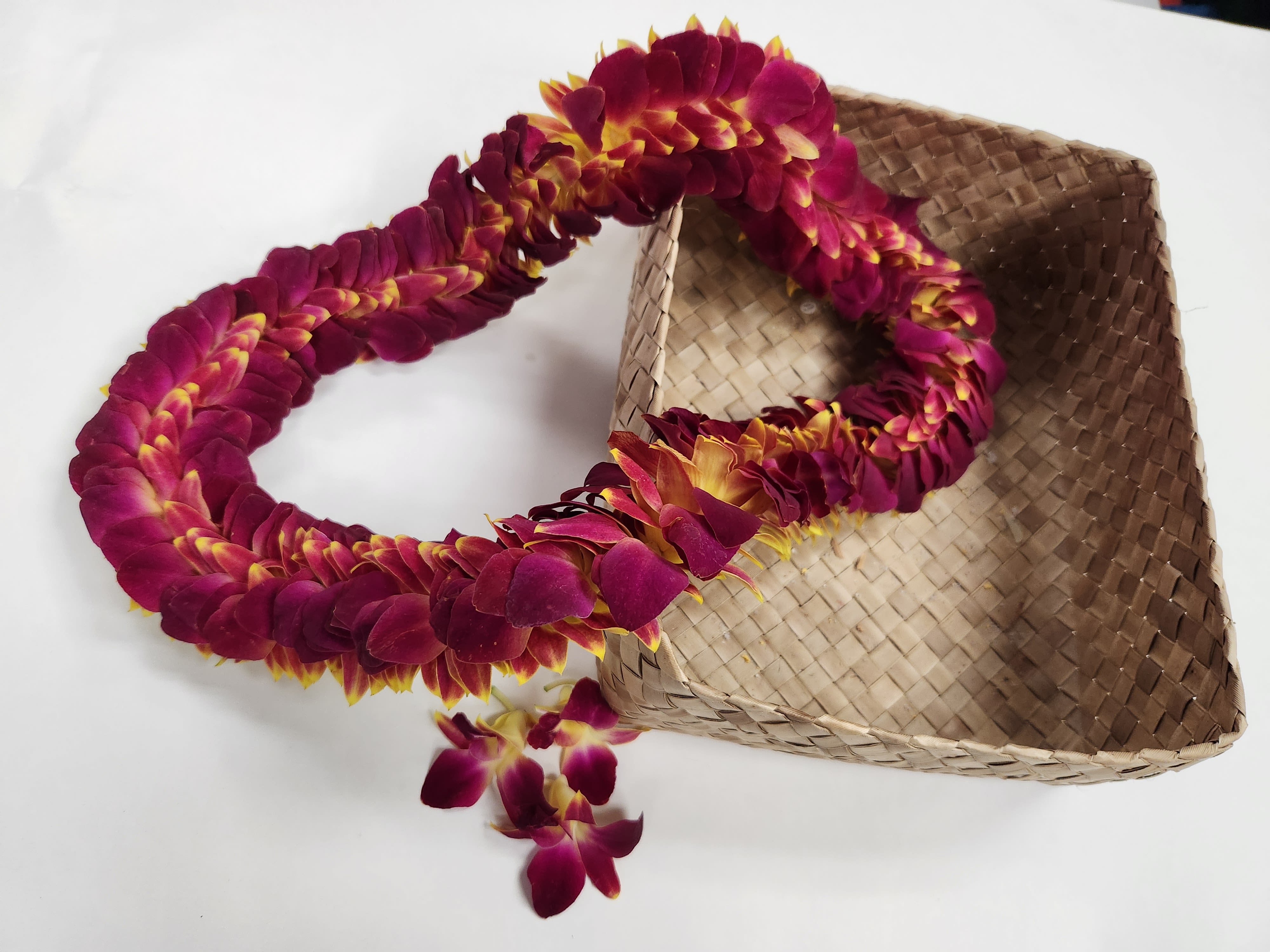 Magenta and yellow flower lei beside a woven straw hat