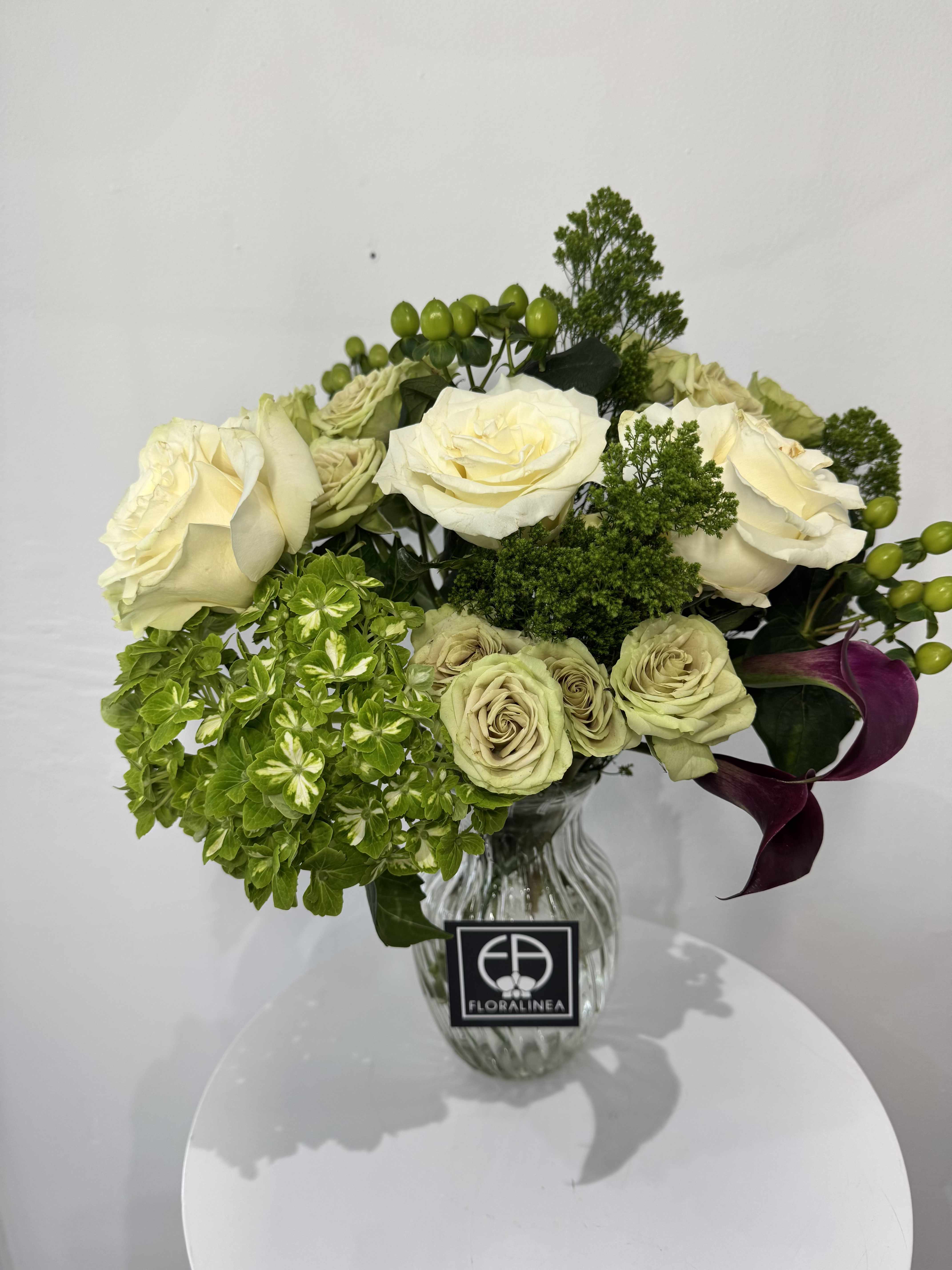 Cream roses and green hydrangea in a glass vase with purple calla lilies