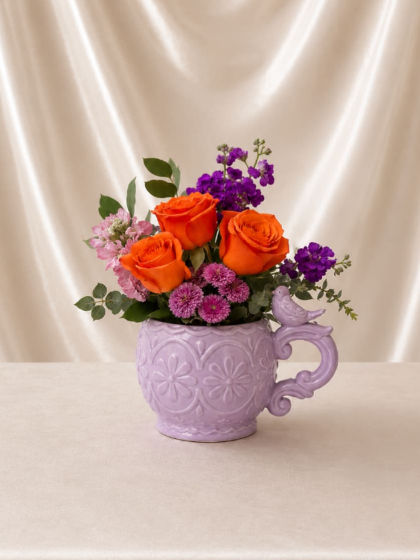 Orange roses and purple flowers in a lavender mug vase
