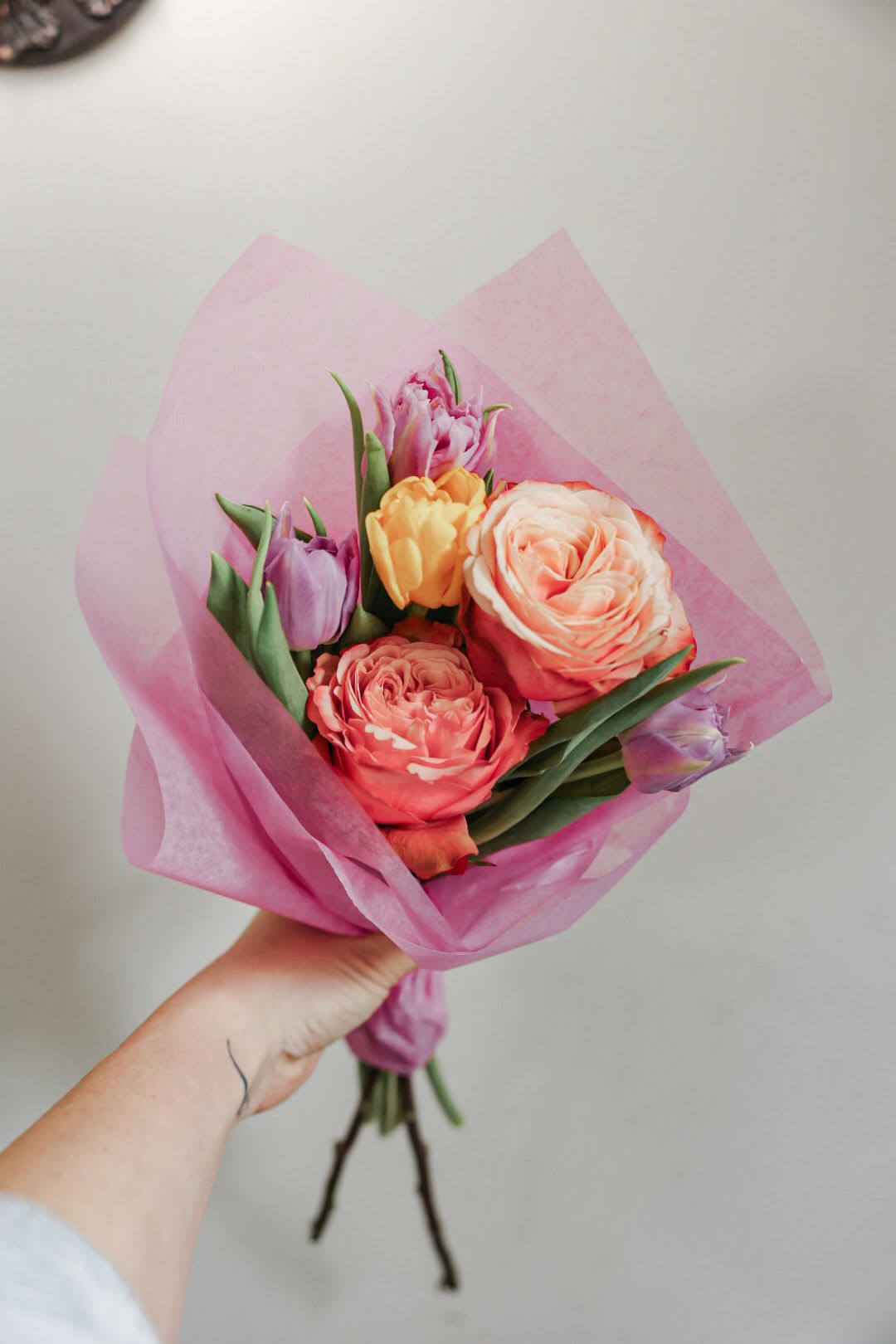 Handheld bouquet of pink and peach tulips wrapped in pink paper