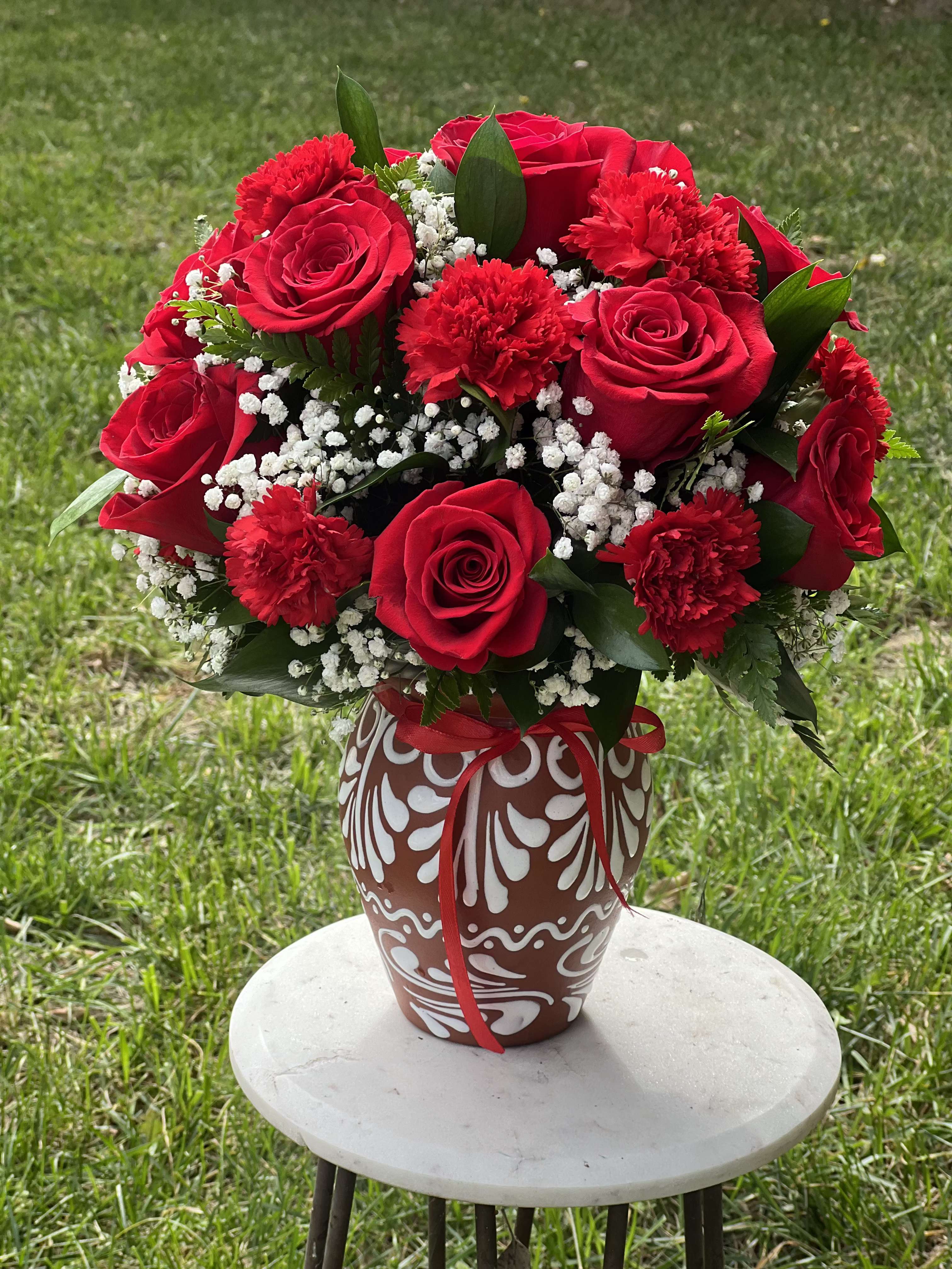 Midnight in Madrid - Captured in the "Midnight in Madrid" arrangement is the timeless romance of a moonlit garden, blending classic elegance with a touch of artisanal charm. Deep, velvety red roses and lush carnations take center stage, beautifully contrasted by delicate clouds of white baby’s breath that mimic stars against a twilight sky. Housed in a hand-painted, terracotta-style vase with traditional motifs, this bouquet offers a refined, heritage-inspired aesthetic perfect for anniversaries, romantic gestures, or as a bold statement piece for a Santa Barbara home. It’s an unforgettable gift that combines high-end floral design with the warm, sun-drenched soul of a Mediterranean evening.