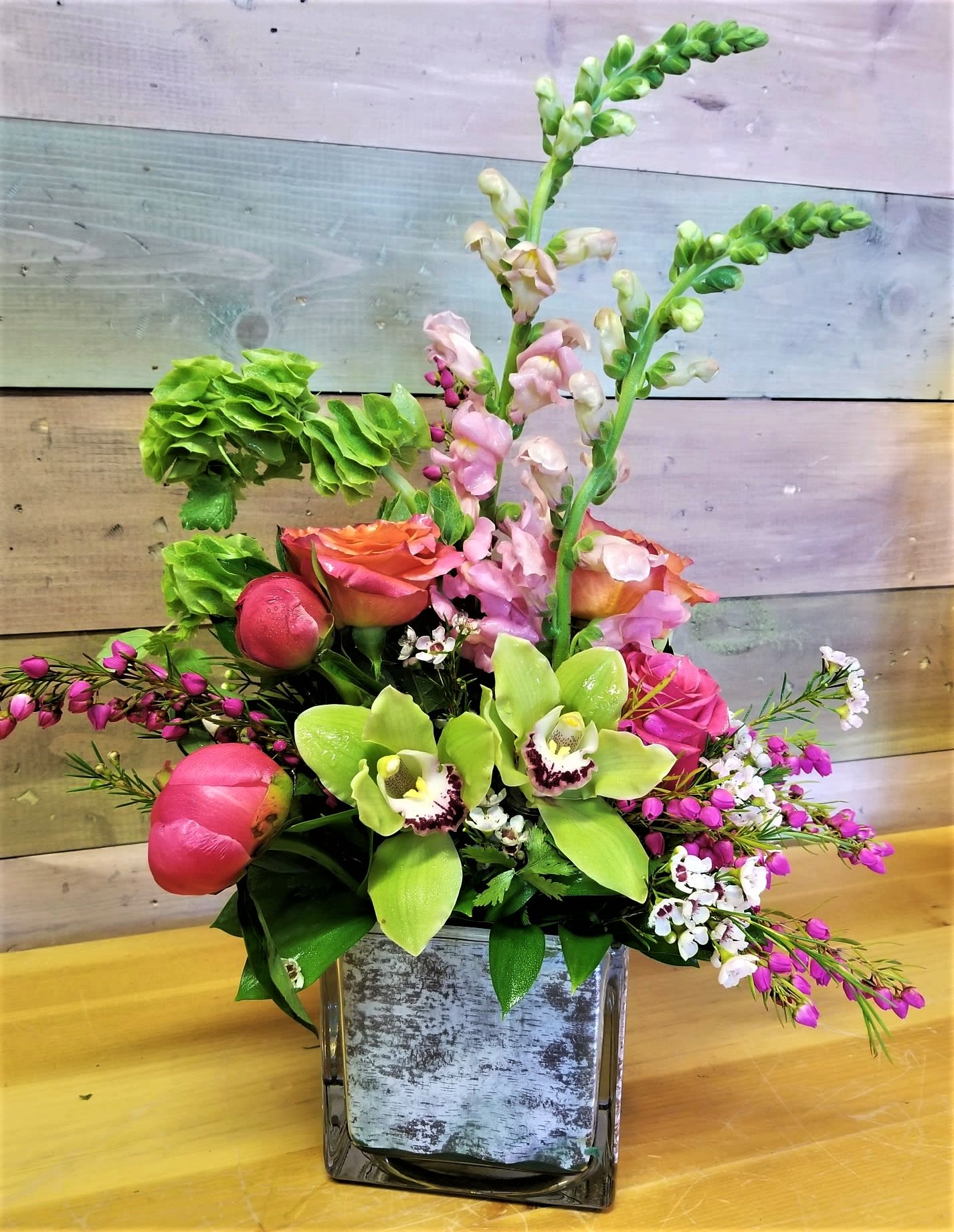 Mixed floral arrangement in a square glass vase with pink and green blooms