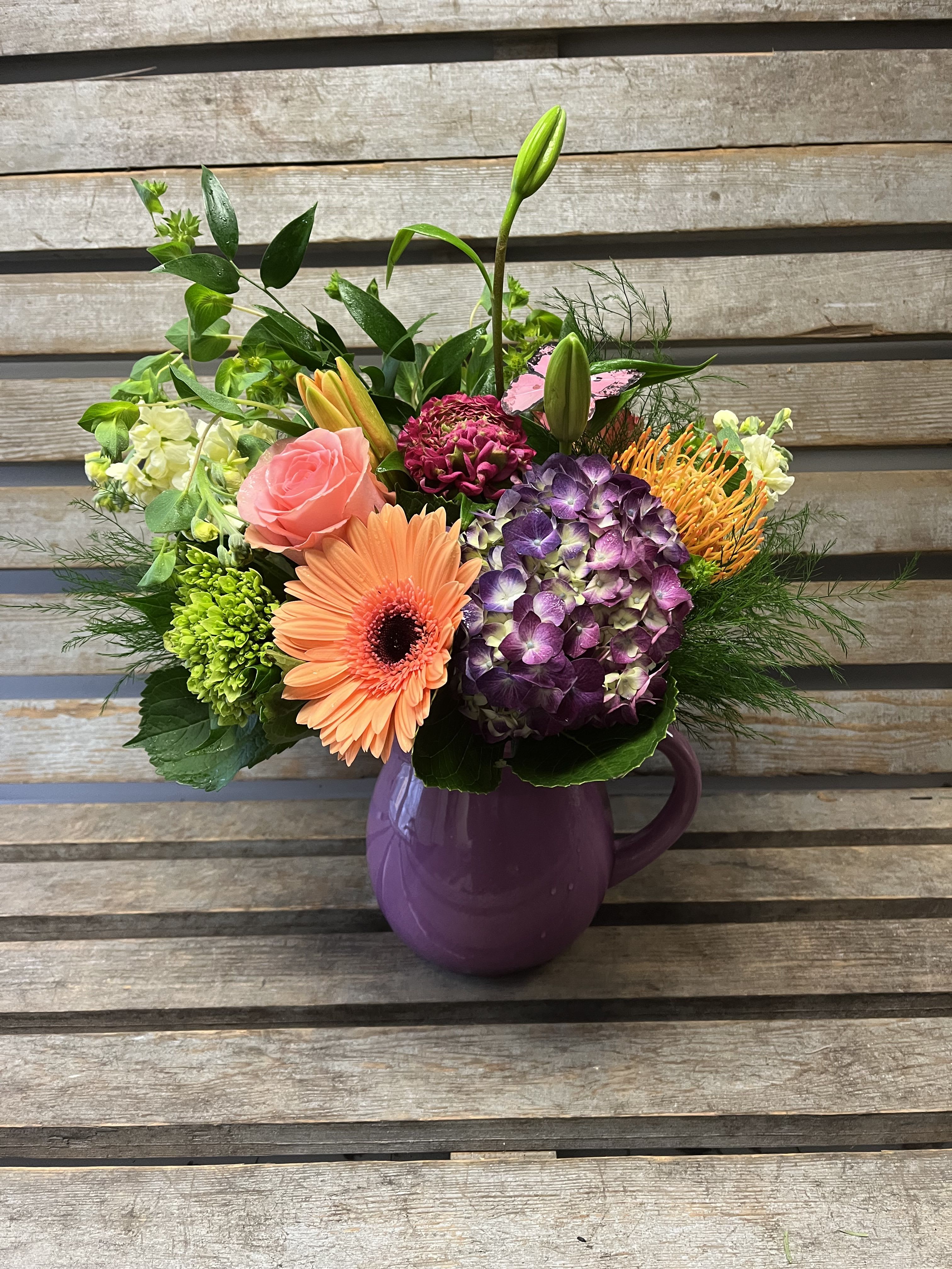 Mixed bouquet in a purple pitcher vase with pink, orange, and purple blooms