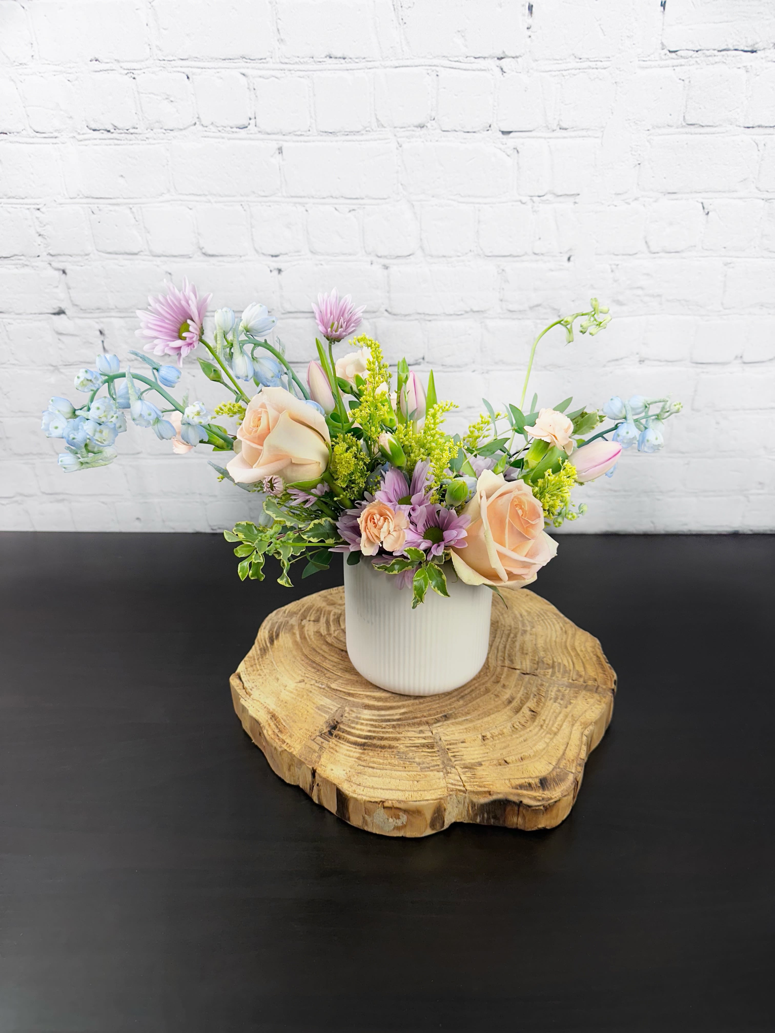 Pastel flower arrangement in a white vase on a wood slice