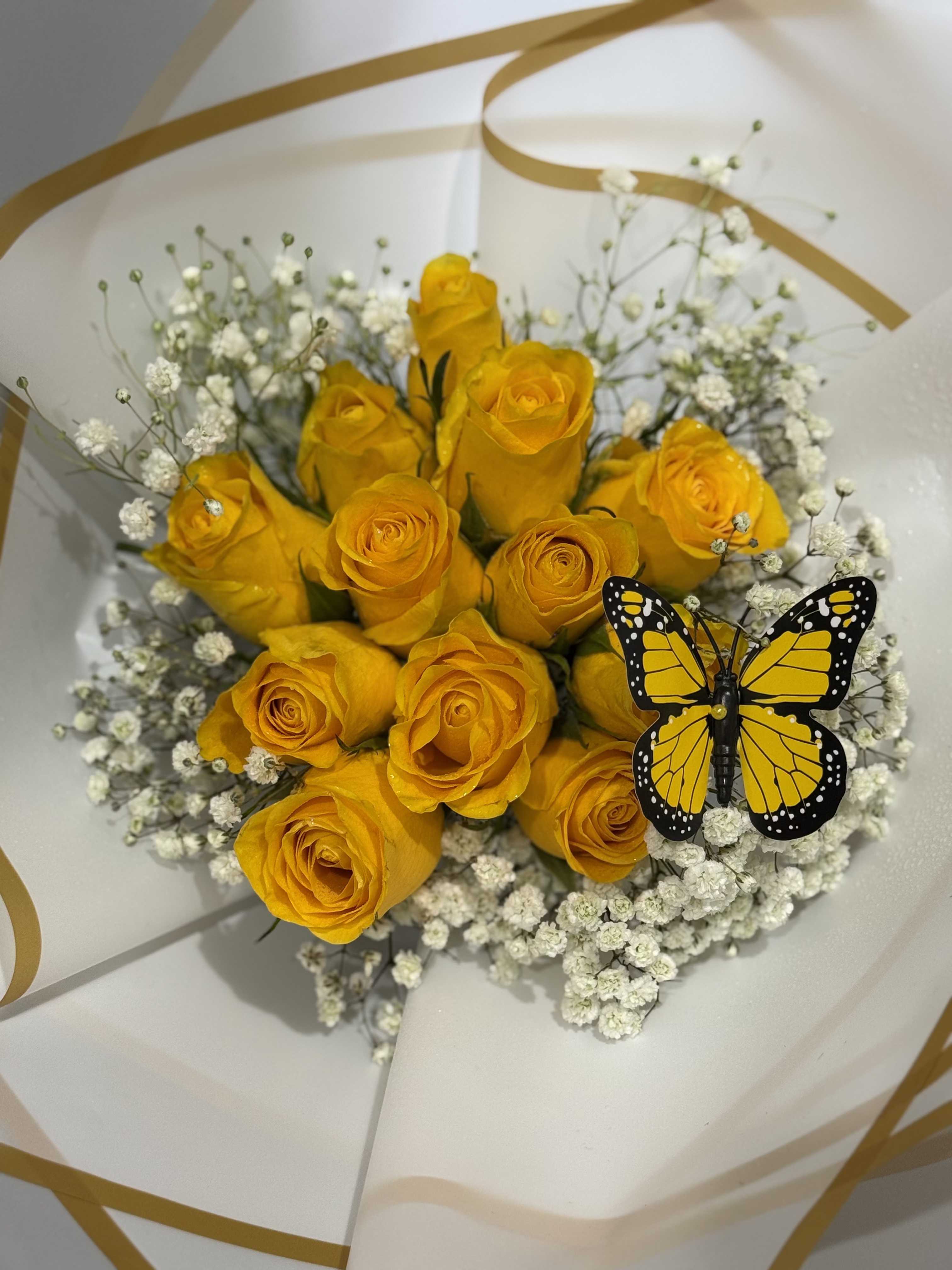 YELLOW BUCHONE  - A cluster of sunlit yellow roses takes center stage in this cheerful flower arrangement, a perfect birthday bouquet or congratulations gift that reads joyful at first glance. The bright roses are paired with airy white baby's breath for high-contrast texture, while a playful black-and-yellow decorative butterfly adds a whimsical, celebratory accent that will make the recipient smile.  Wrapped in crisp white paper with elegant gold curved accents, the presentation feels polished and ready to gift-ideal for sending to someone who deserves a sunny pick-me-up or to mark a happy milestone. The mix of yellow, white, and black tones creates a modern yet warm look; arrange will arrive as shown with the butterfly and bouquet wrap, and recipients will find the stems easy to unpack and display.