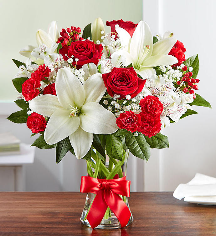 Red roses and white lilies in a clear glass vase with a red ribbon.