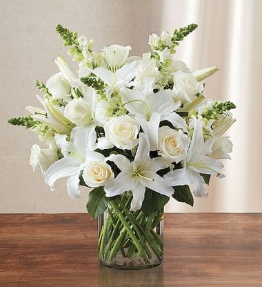 Arrangement of white lilies, roses, and snapdragons in a clear glass cylinder vase