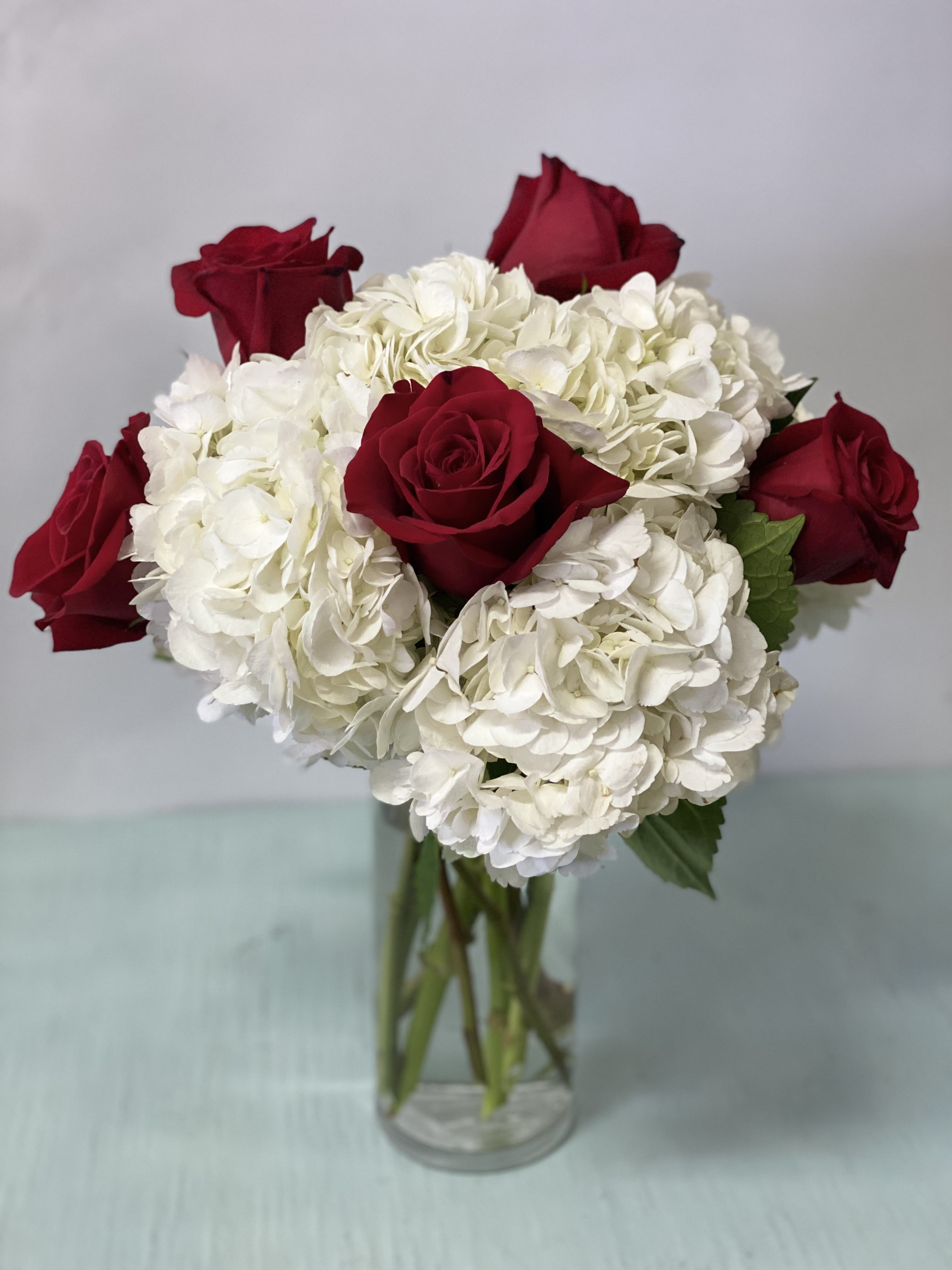 Red roses with white hydrangeas in a clear glass vase
