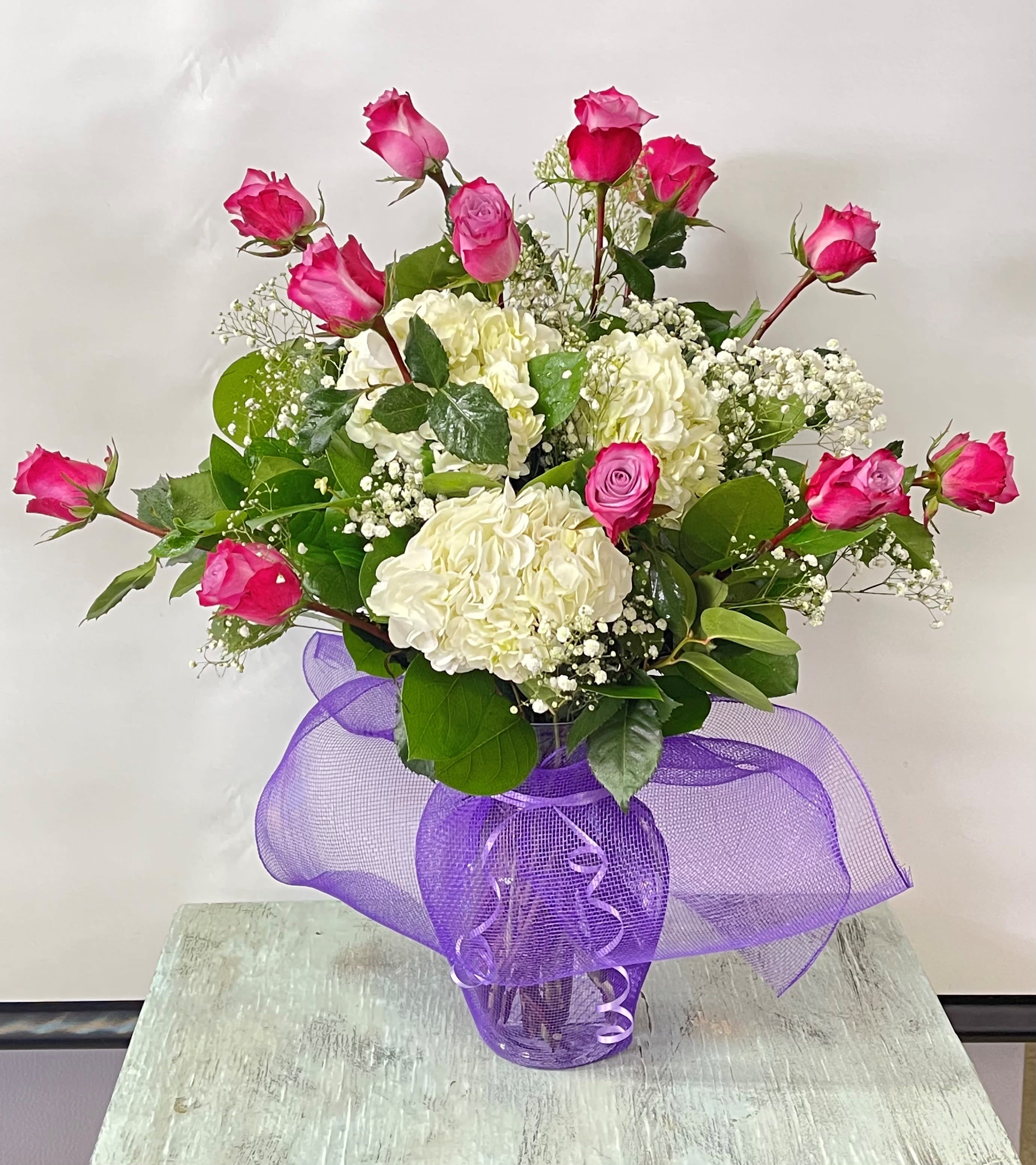 Pink roses and white hydrangeas in a glass vase with purple ribbon