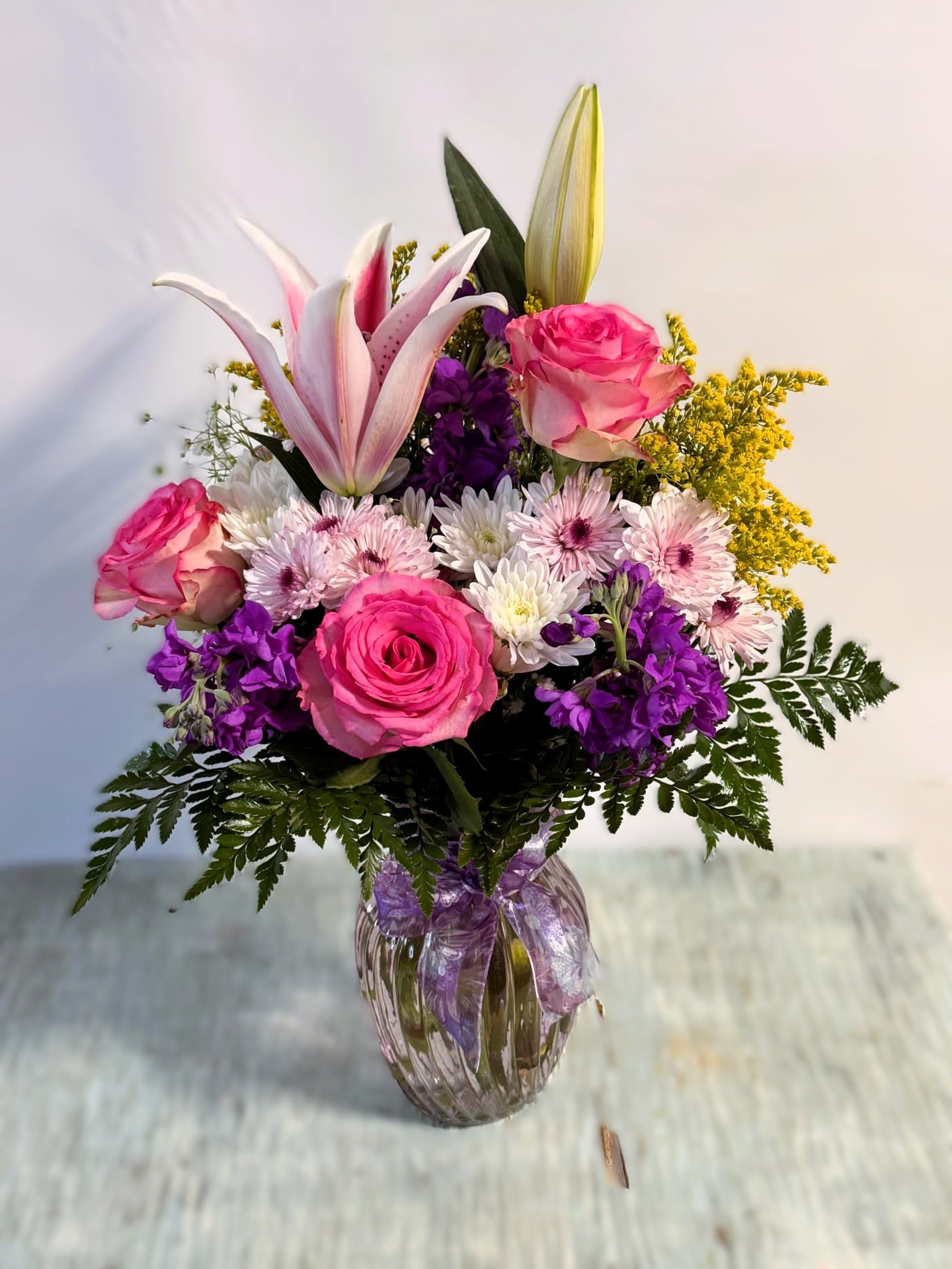 Bouquet of pink roses, lilies, and purple flowers in a glass vase