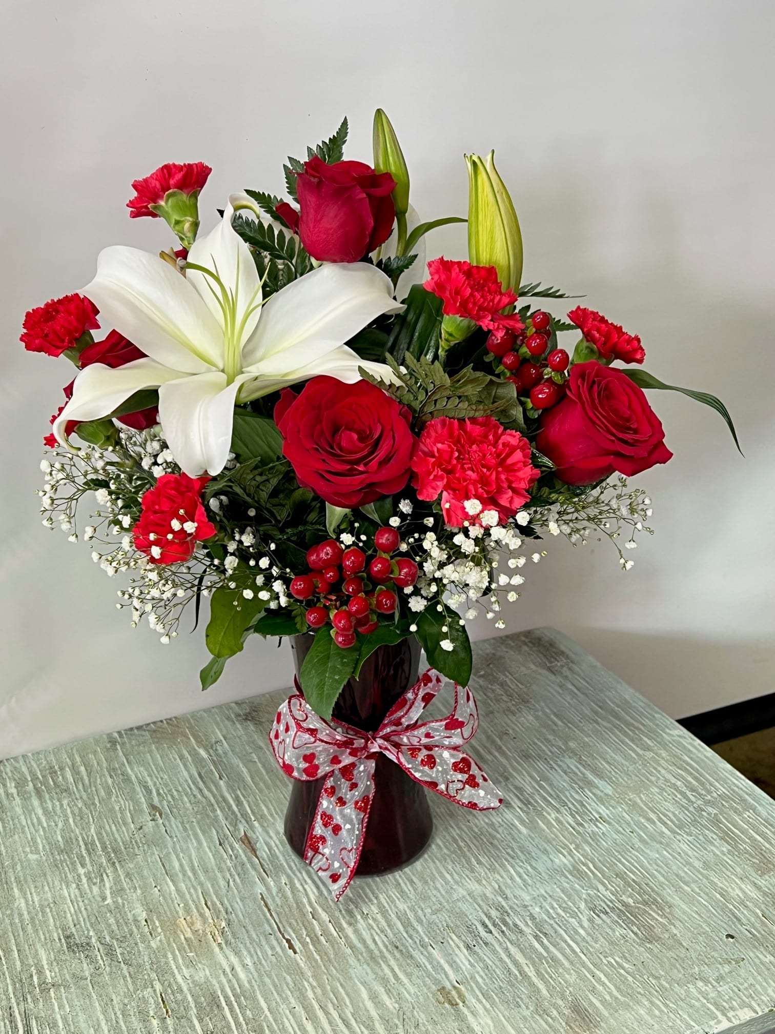 Red roses and white lilies in a dark vase with a heart ribbon