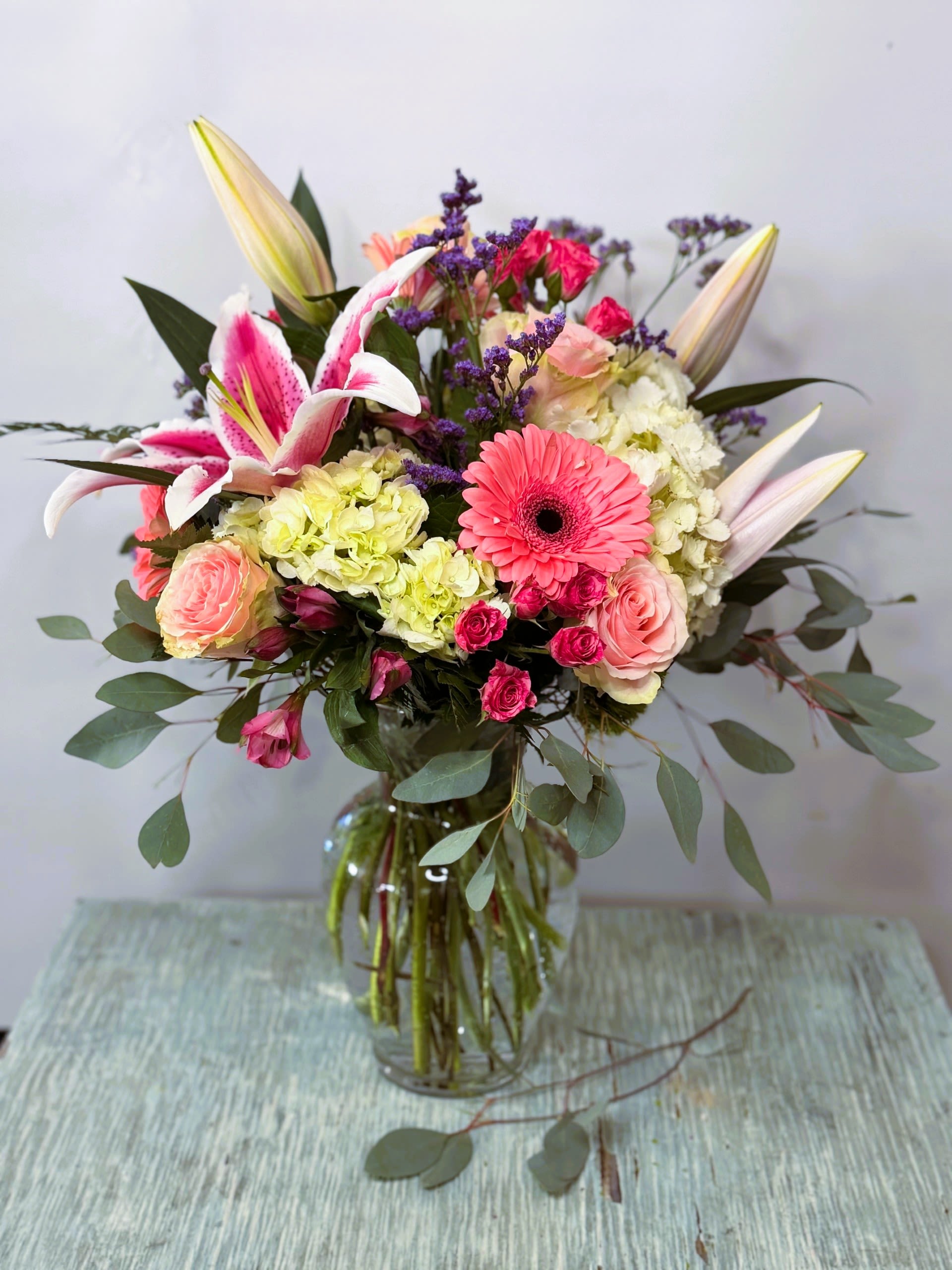 Mixed bouquet in a glass vase with pink lilies, roses, and a gerbera daisy