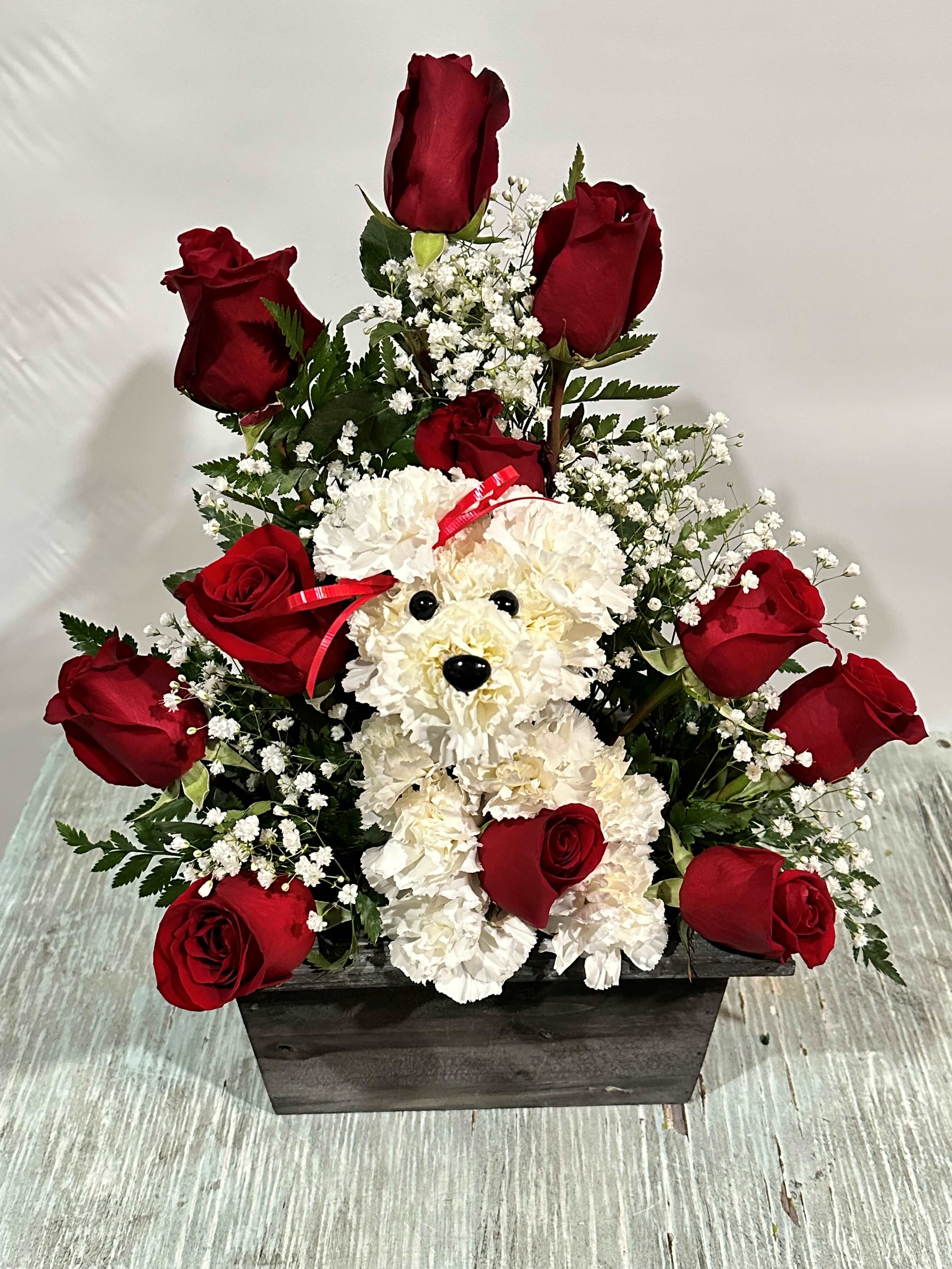 Red roses arranged around a white teddy bear in a wooden box