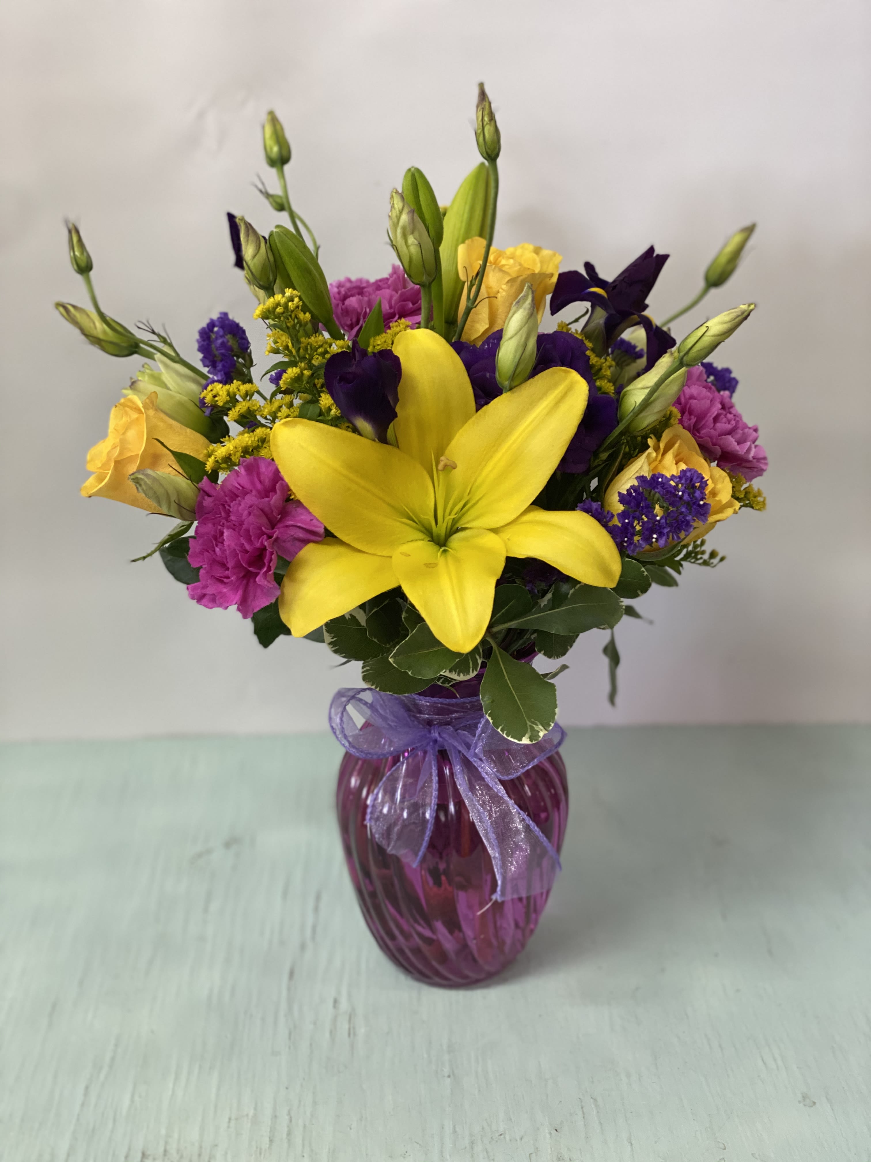 Bouquet of yellow lilies, purple flowers, and pink carnations in a purple vase