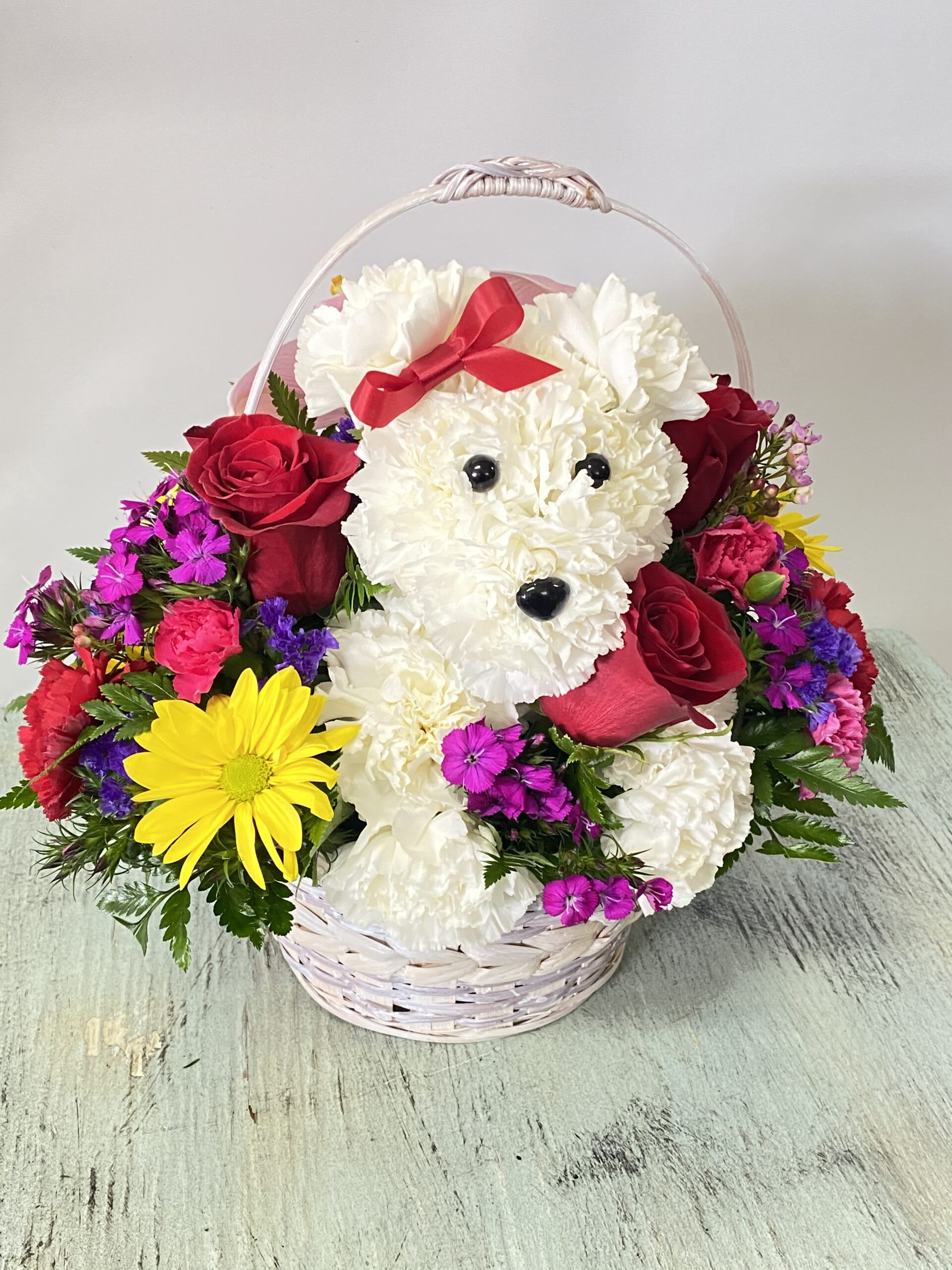 Flower basket with a white teddy bear face, red roses, and bright mixed blooms