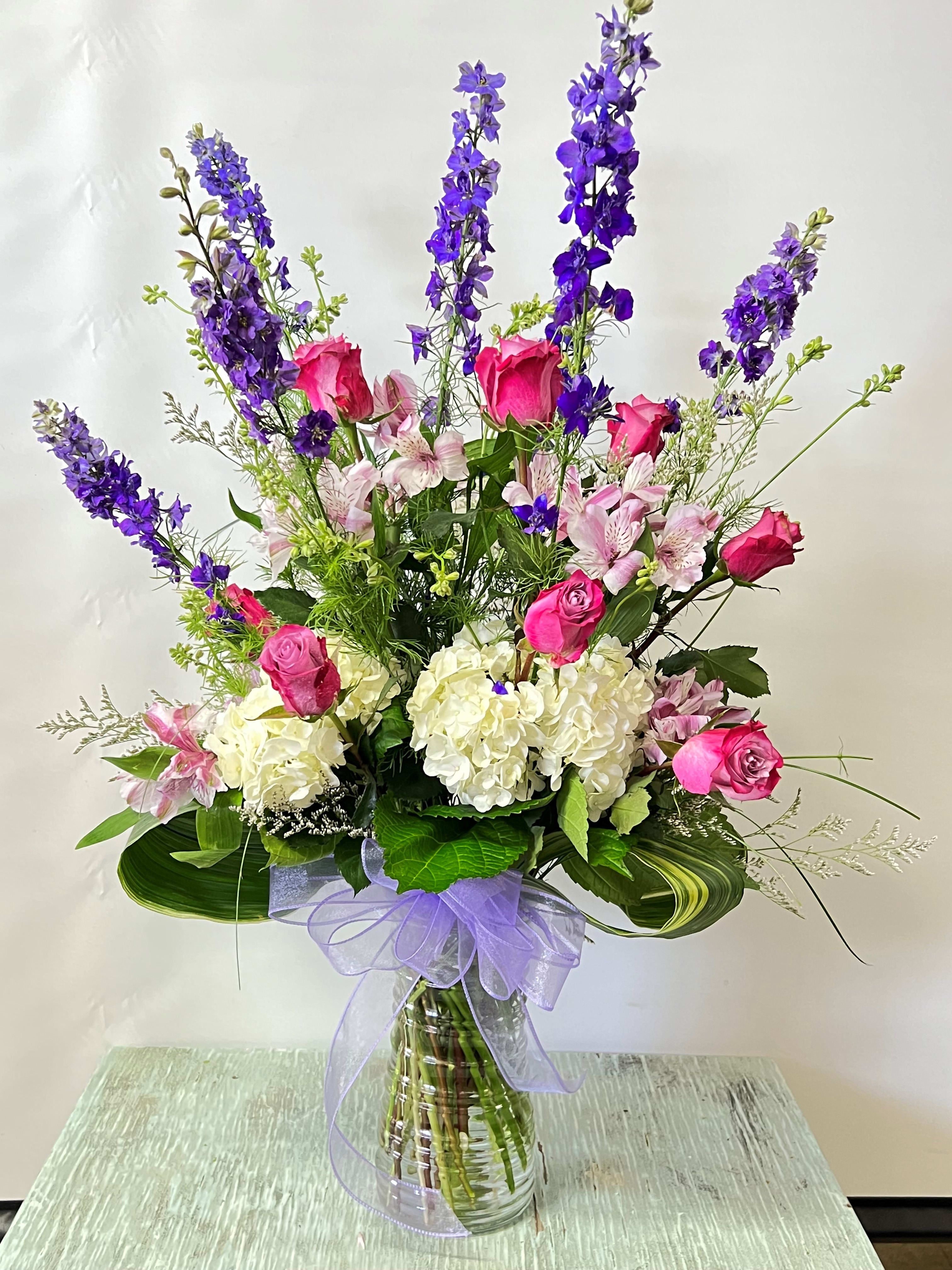 Tall bouquet of pink roses, white hydrangeas, and purple delphinium in a glass vase