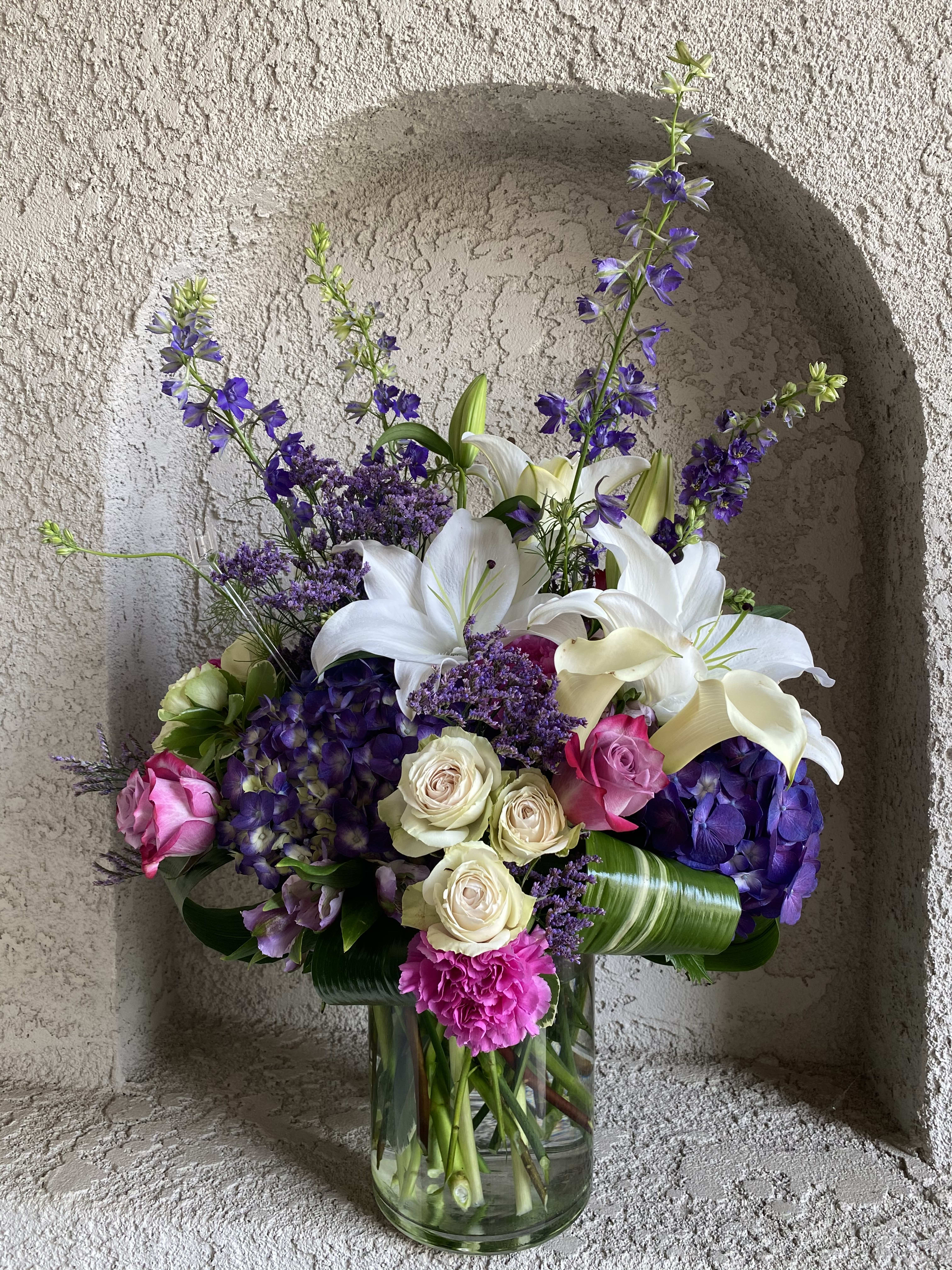Bouquet of white lilies, purple flowers, and pink roses in a glass vase