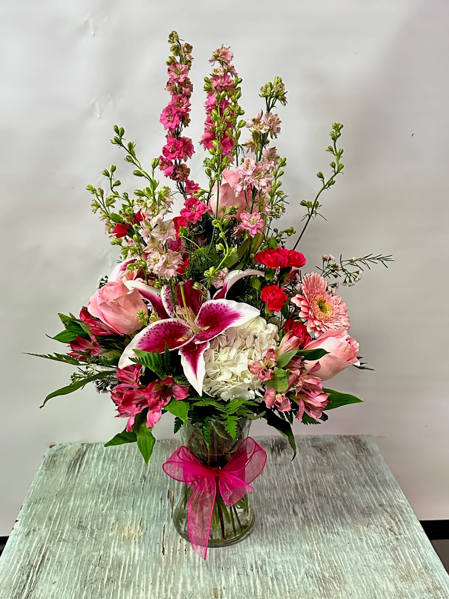 Pink and white mixed flower arrangement in a glass vase with a pink ribbon