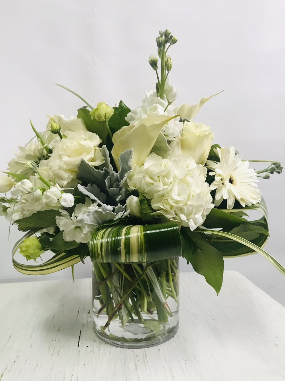 White floral arrangement in a clear glass vase with a striped leaf wrap
