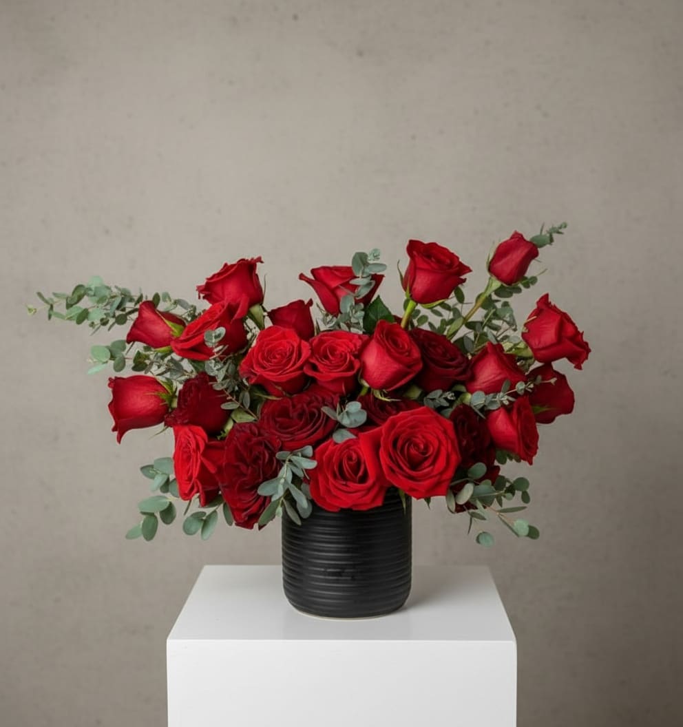 Red roses arranged in a black vase with eucalyptus accents