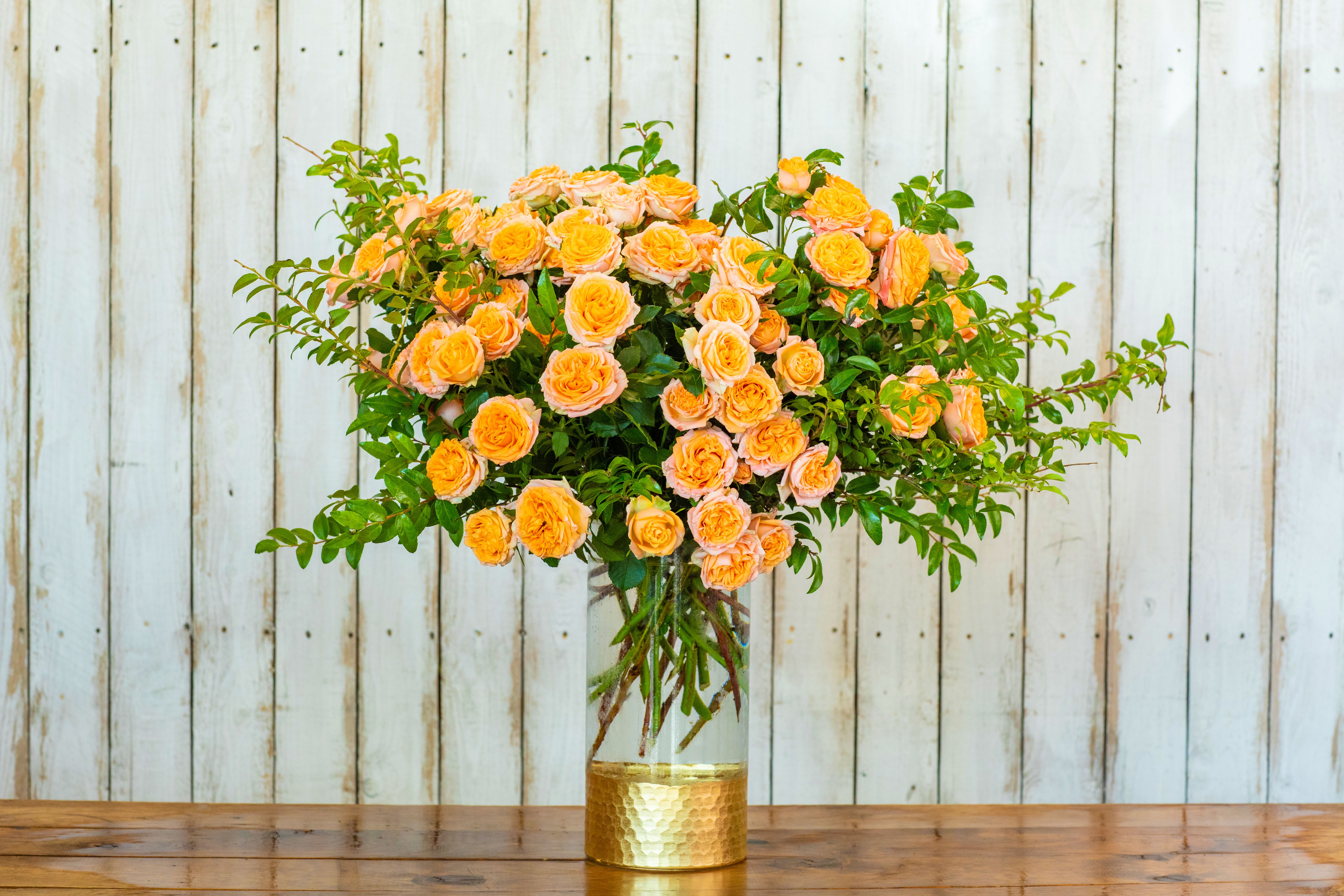 Orange Sunset Rose Dream - Illuminate any occasion with the Orange Sunset Rose Dream, a spectacular arrangement from your dedicated Rancho Cucamonga Florist. This breathtaking bouquet features a lavish display of vibrant orange spray roses, brimming with warmth, enthusiasm, and energy. The striking baby spray roses are perfectly complemented by rich, trailing green foliage, creating an arrangement that is both expansive and absolutely stunning.  The bouquet is beautifully presented in a clear glass vase, accented with a stylish gold-textured base, adding a modern touch of elegance. This luxurious presentation makes the arrangement a truly memorable gift.  As the leading Rancho Cucamonga flower shop, we take pride in delivering farm-fresh, high-quality blooms. The Orange Sunset Rose Dream is the perfect choice for celebrating milestones like an important birthday bouquet, a jubilant graduation gift, a passionate anniversary surprise, or as unique get well flowers.  We offer dependable same-day flower delivery throughout the Rancho Cucamonga area, ensuring this gorgeous arrangement arrives fresh and ready to impress. For the most beautiful, vibrant roses, trust your local expert. Order this extraordinary floral arrangement online today from your reliable Rancho Cucamonga Florist!