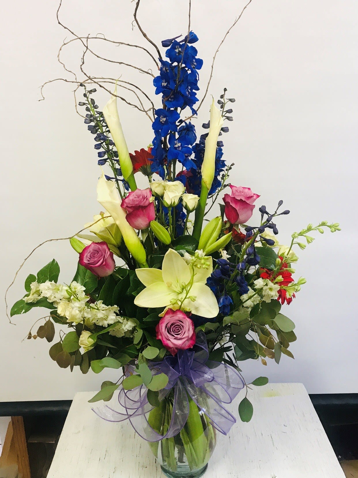 Tall mixed bouquet with blue, pink, white, and red flowers in a glass vase