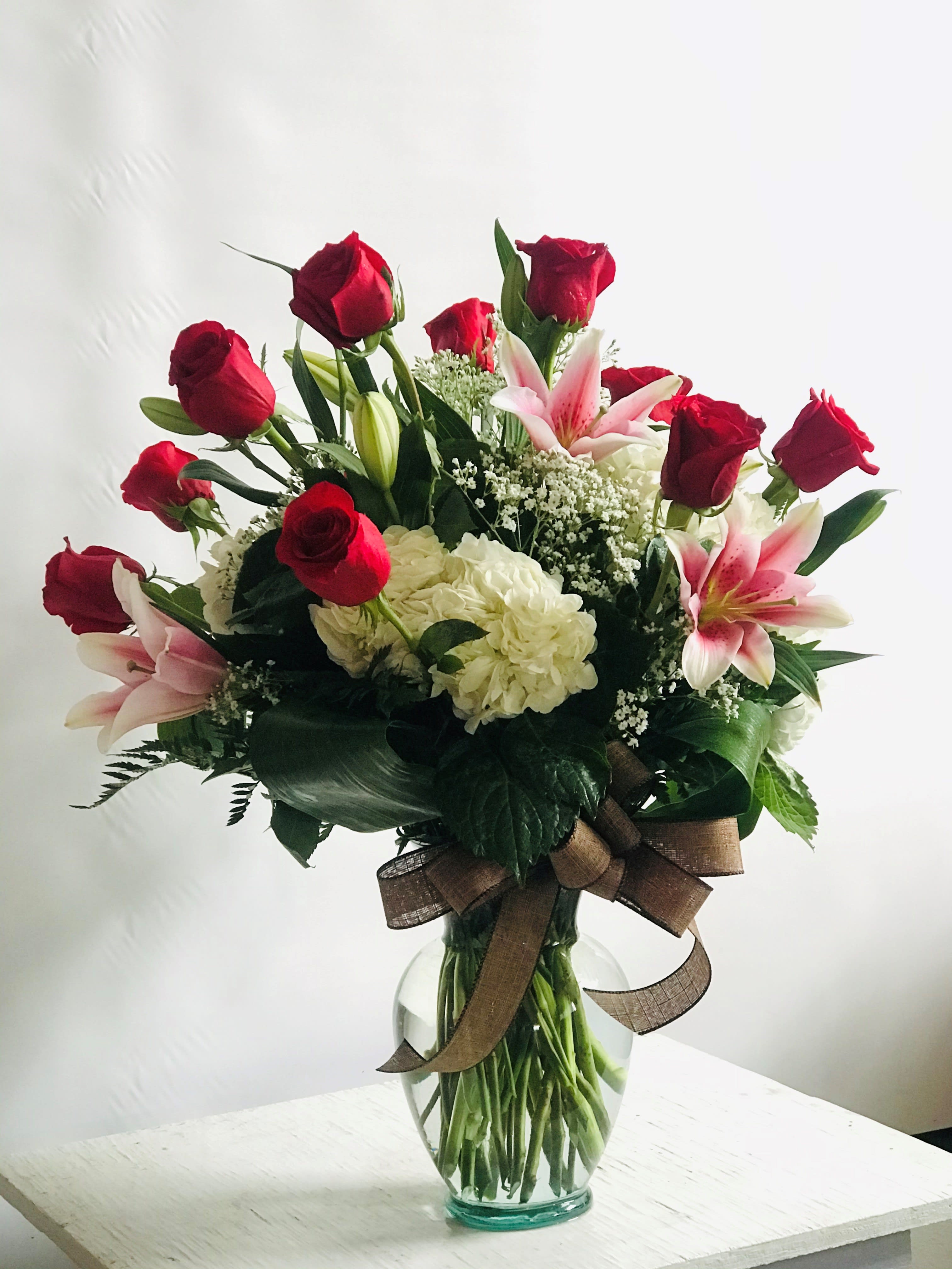 Red roses and pink lilies in a glass vase with a brown ribbon