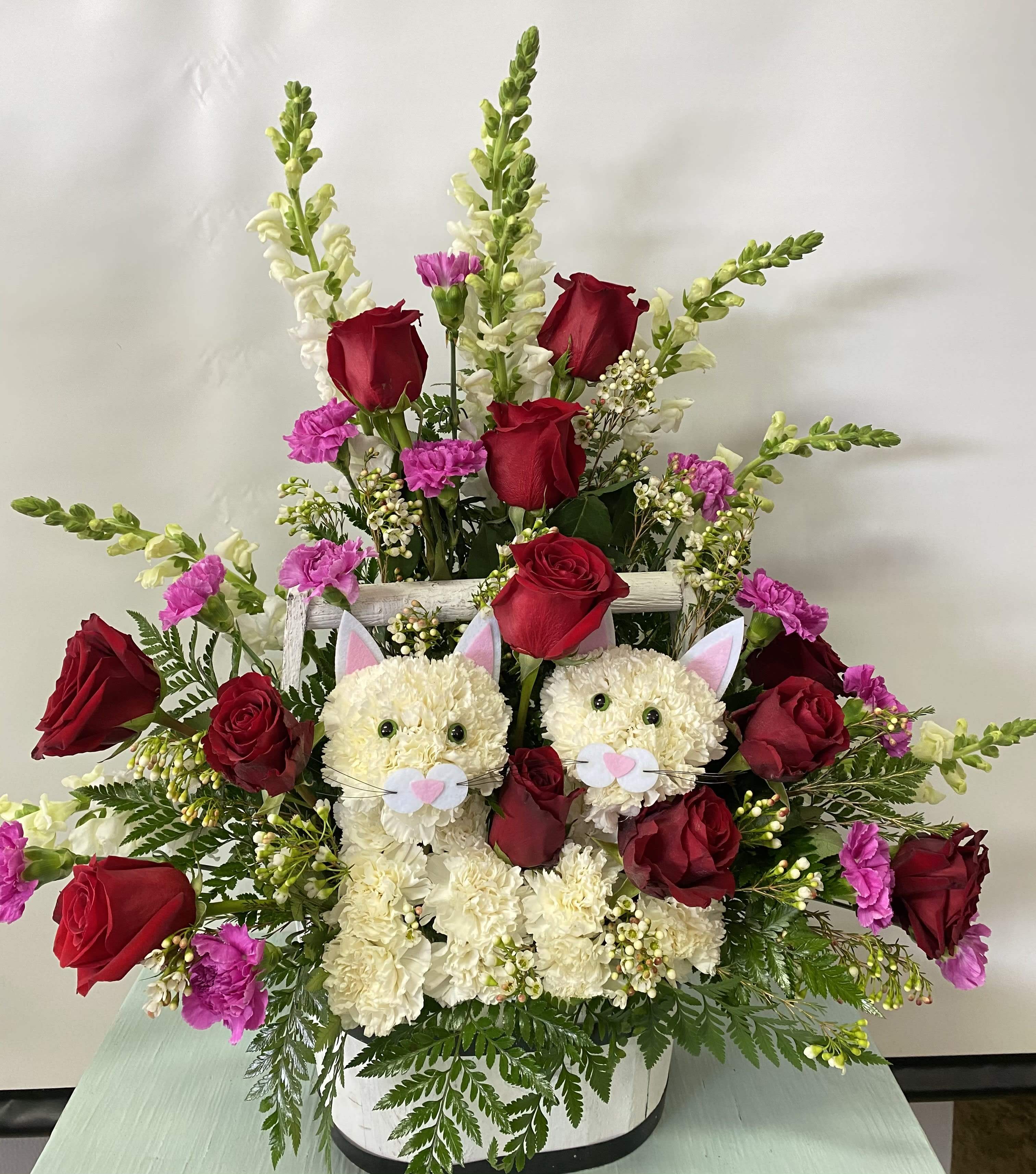 Flower arrangement with red roses and two cat faces in a white basket