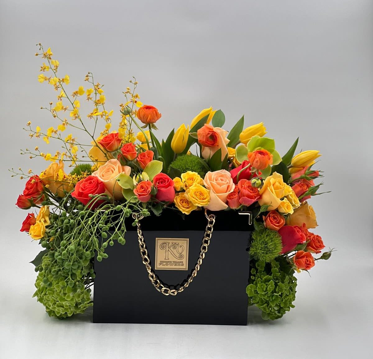 Mother’s Day Golden Garden Handbag - Celebrate Mother’s Day with this vibrant luxury arrangement overflowing fresh seasonal blooms in warm sunset tones. Designed in a sophisticated black handbag container with gold chain accents, this statement piece brings together elegance, joy, and modern garden beauty, a radiant expression of love and appreciation for Mom.