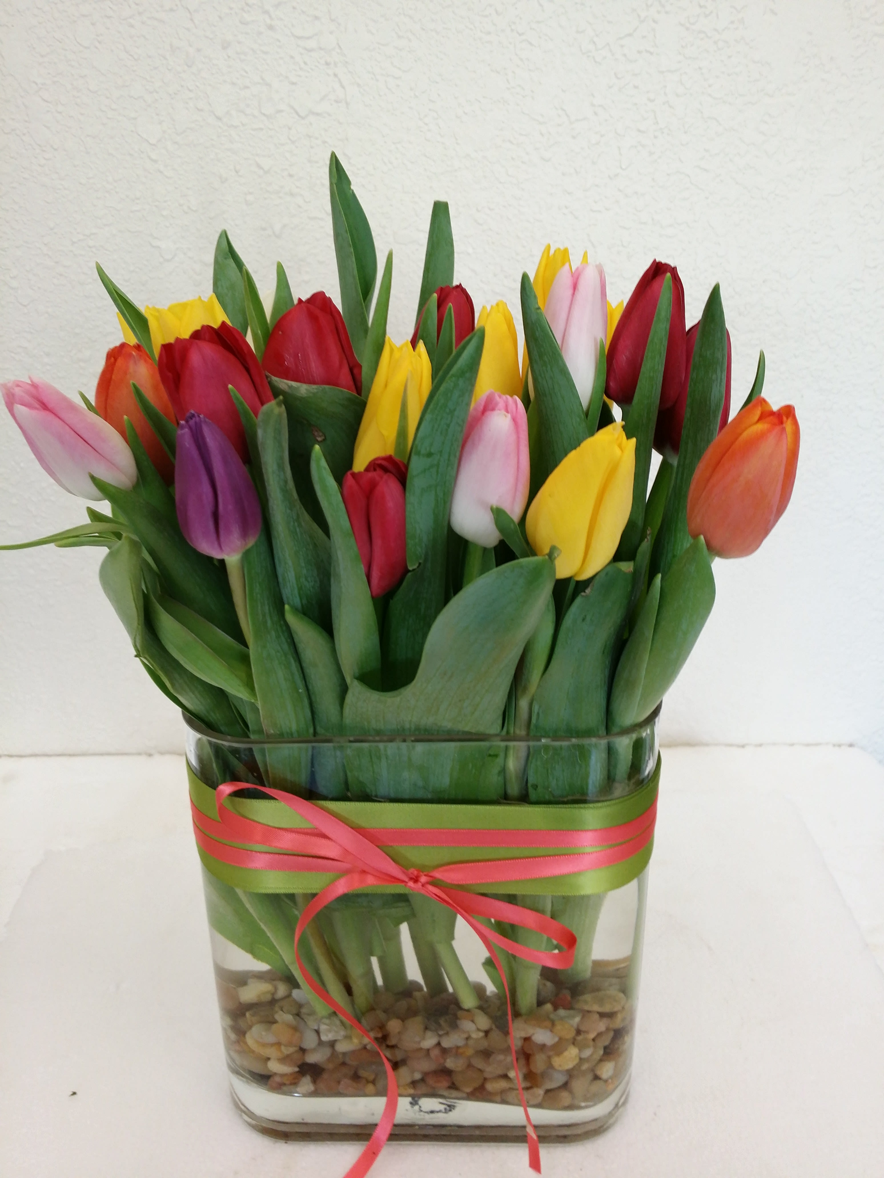 Mixed tulips in a glass vase with a pink ribbon