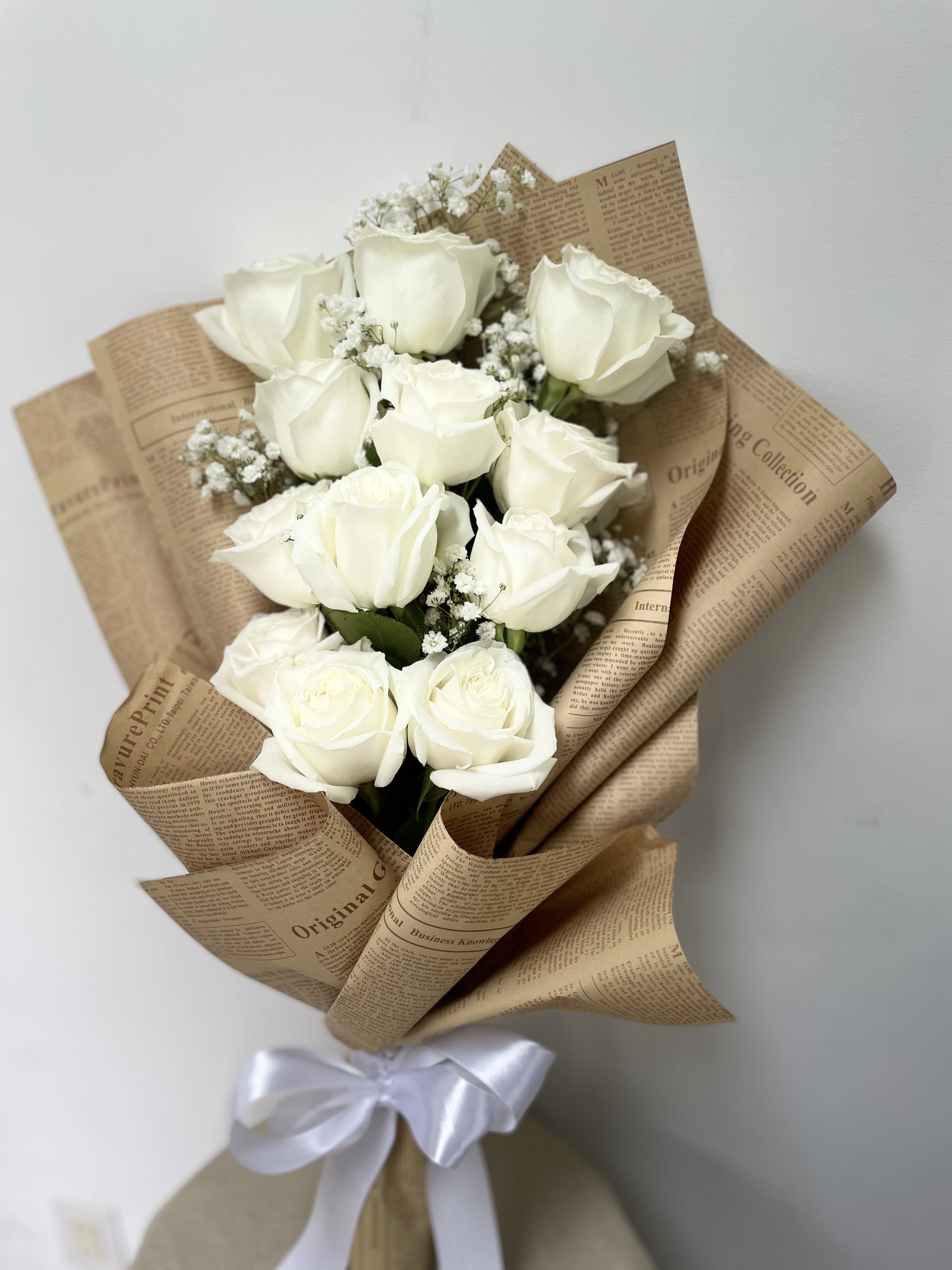Bouquet of white roses wrapped in brown paper with a white ribbon