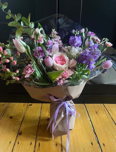 Bouquet of pink and purple flowers wrapped in paper with a lavender ribbon