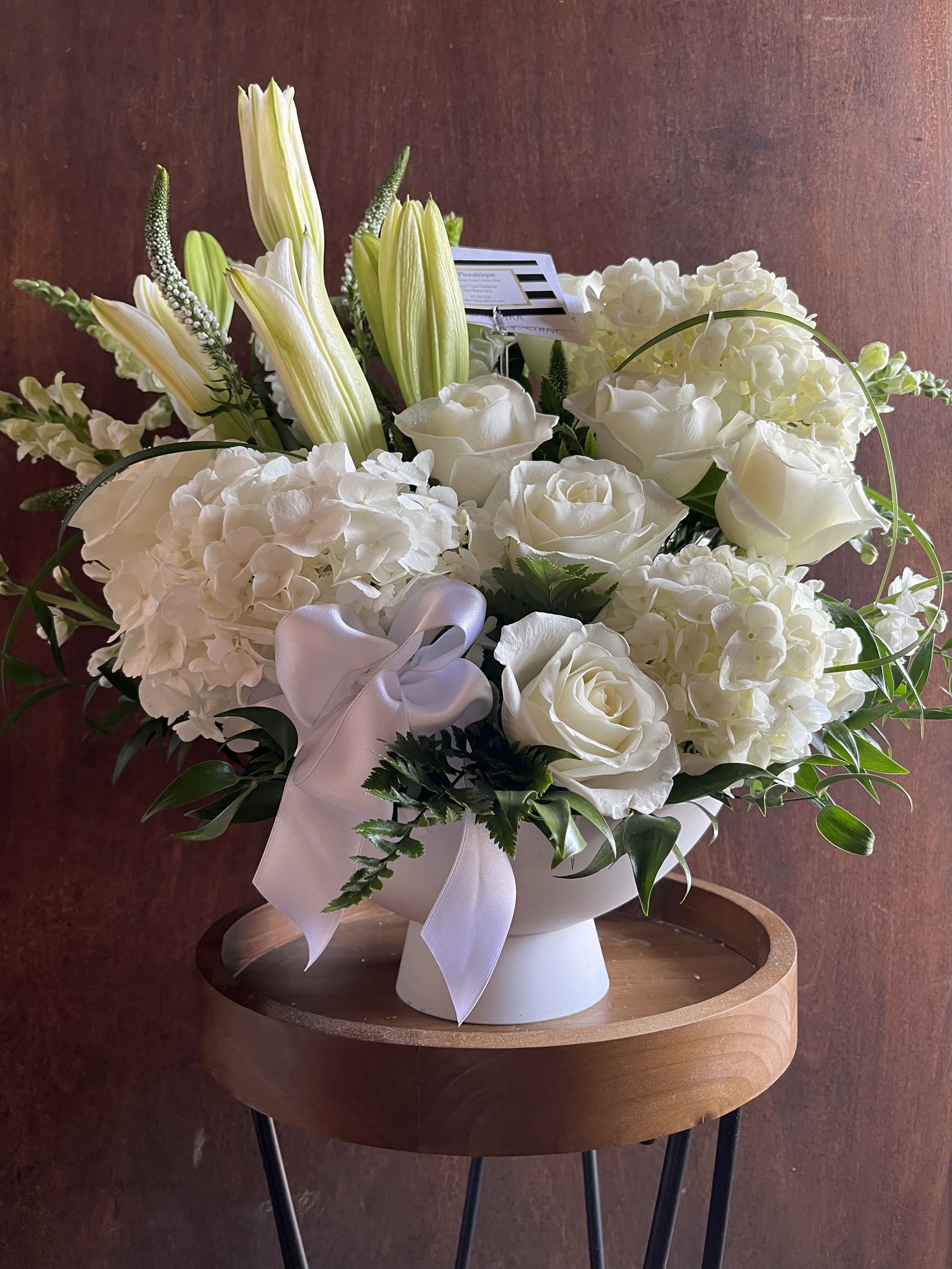 White floral arrangement in a pedestal vase with a lavender ribbon
