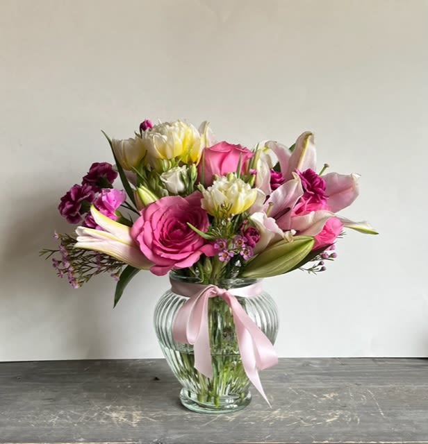 Pink and white mixed bouquet in a clear glass vase with a pink ribbon