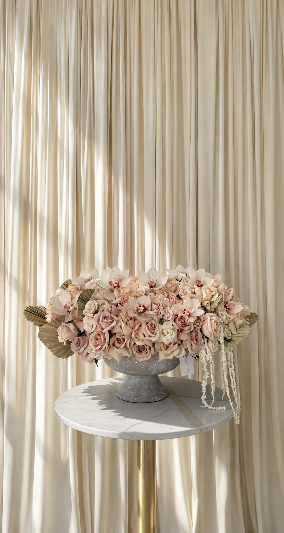 Blushing And Blooming - Blushing &amp; Blooming is a dreamy statement arrangement designed to feel soft, romantic, and effortlessly luxurious. Overflowing with delicate blush roses, creamy ivory blooms, elegant white orchids, and cascading floral textures, this arrangement captures the beauty of modern romance in full bloom. Designed in a sophisticated stone vessel with layered neutral tones and airy movement, every detail feels refined yet playful. Perfect for Mother’s Day, birthdays, celebrations, or simply making someone feel adored, Blushing and Blooming brings a graceful, feminine charm to any space while creating the ultimate luxury floral moment.