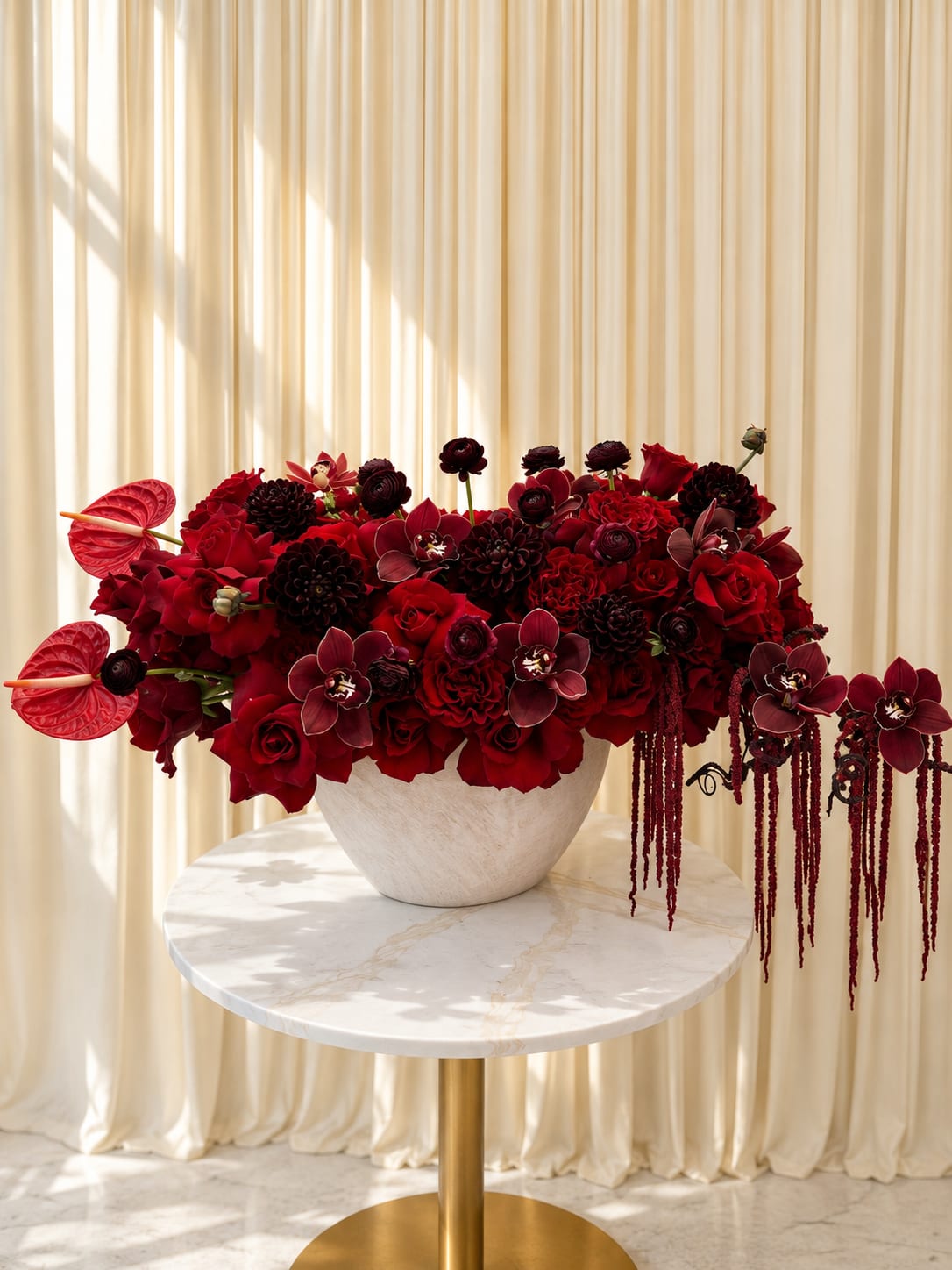 Rouge Romance - Rouge Romance is a bold and luxurious floral arrangement designed to capture the essence of passion, elegance, and timeless romance. Overflowing with rich crimson roses, velvety burgundy blooms, cascading orchids, and dramatic textural accents, this arrangement creates a striking statement from every angle. Designed in an elegant ceramic vessel with layered deep red tones and soft romantic movement, Rouge Romance blends modern luxury with classic sophistication. Perfect for anniversaries, romantic gestures, celebrations, or elevating any space with a touch of opulence, this arrangement embodies beauty, confidence, and unforgettable romance.