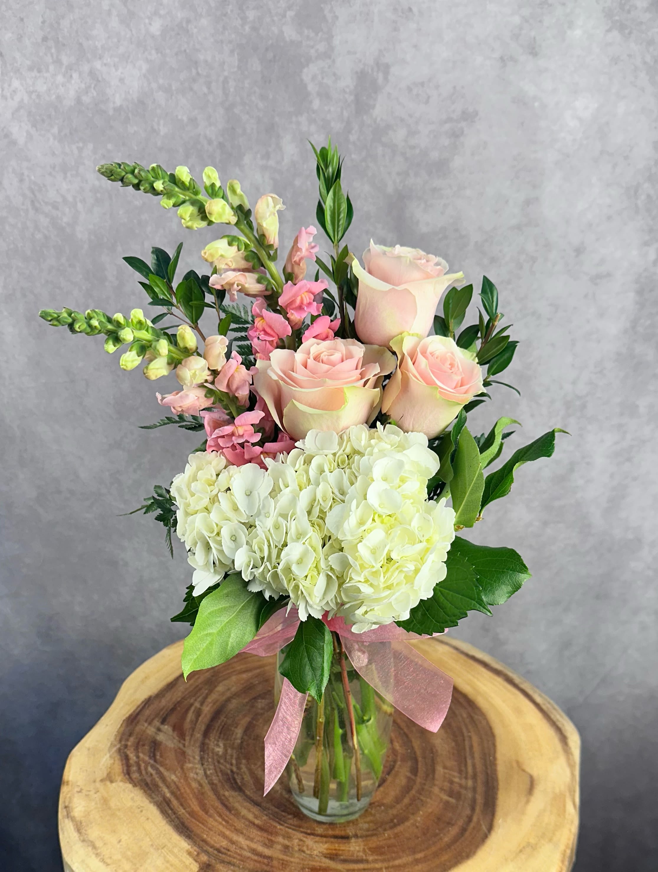 Mama Mia - Featuring classic roses, a full hydrangea, and elegant snapdragons, "Mama Mia" blends softness with height for a beautifully balanced look. This is a frontal-facing, one sided arrangement, standing approximately 15" high and 9" wide.  Please Note: Standard Delivery for this product occurs in the afternoon, between 2:30pm and 7pm. If you need it by a certain time, there is an option to select a timed window for scheduled deliveries.
