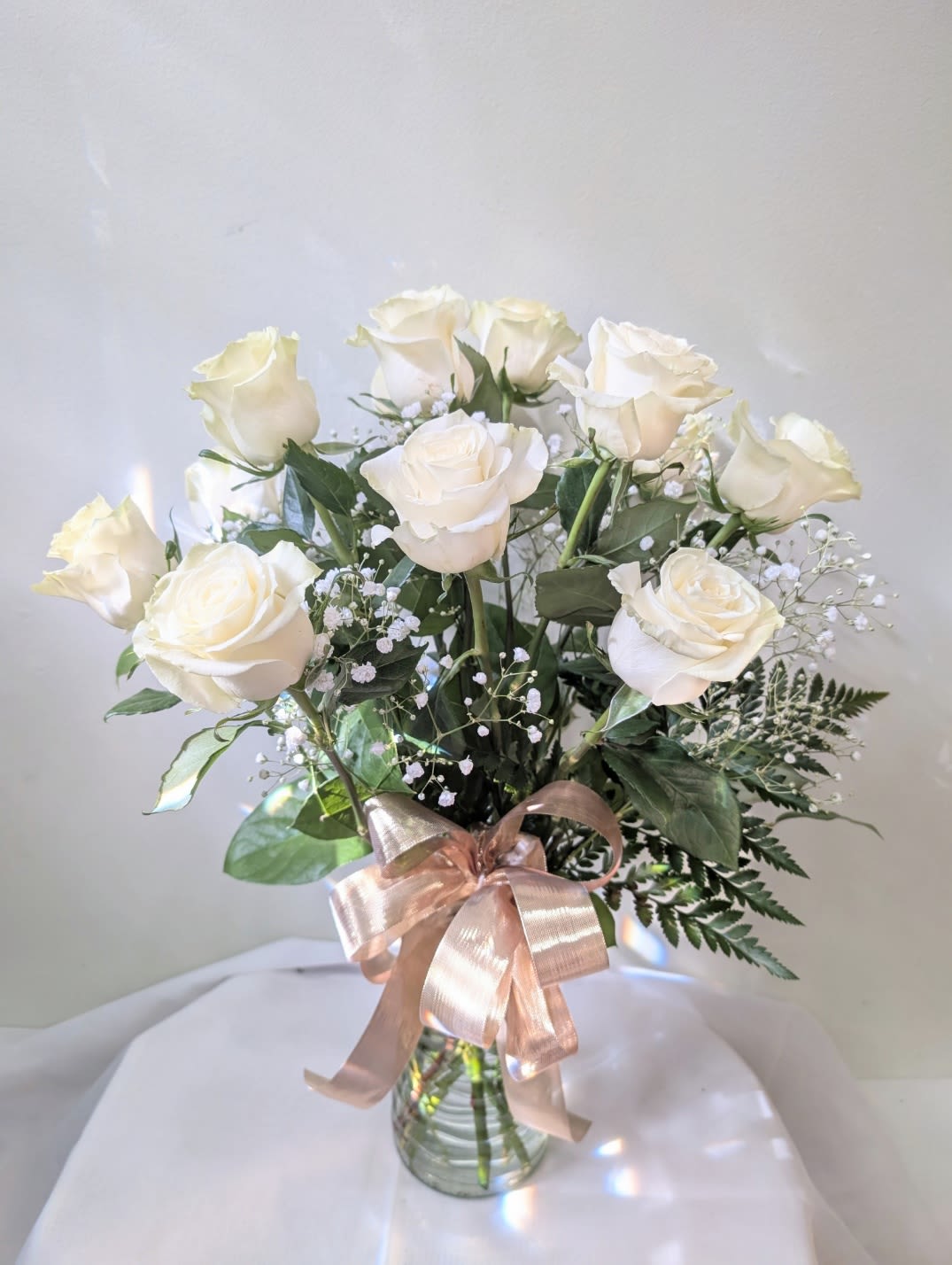 White roses in a glass vase with a pink ribbon
